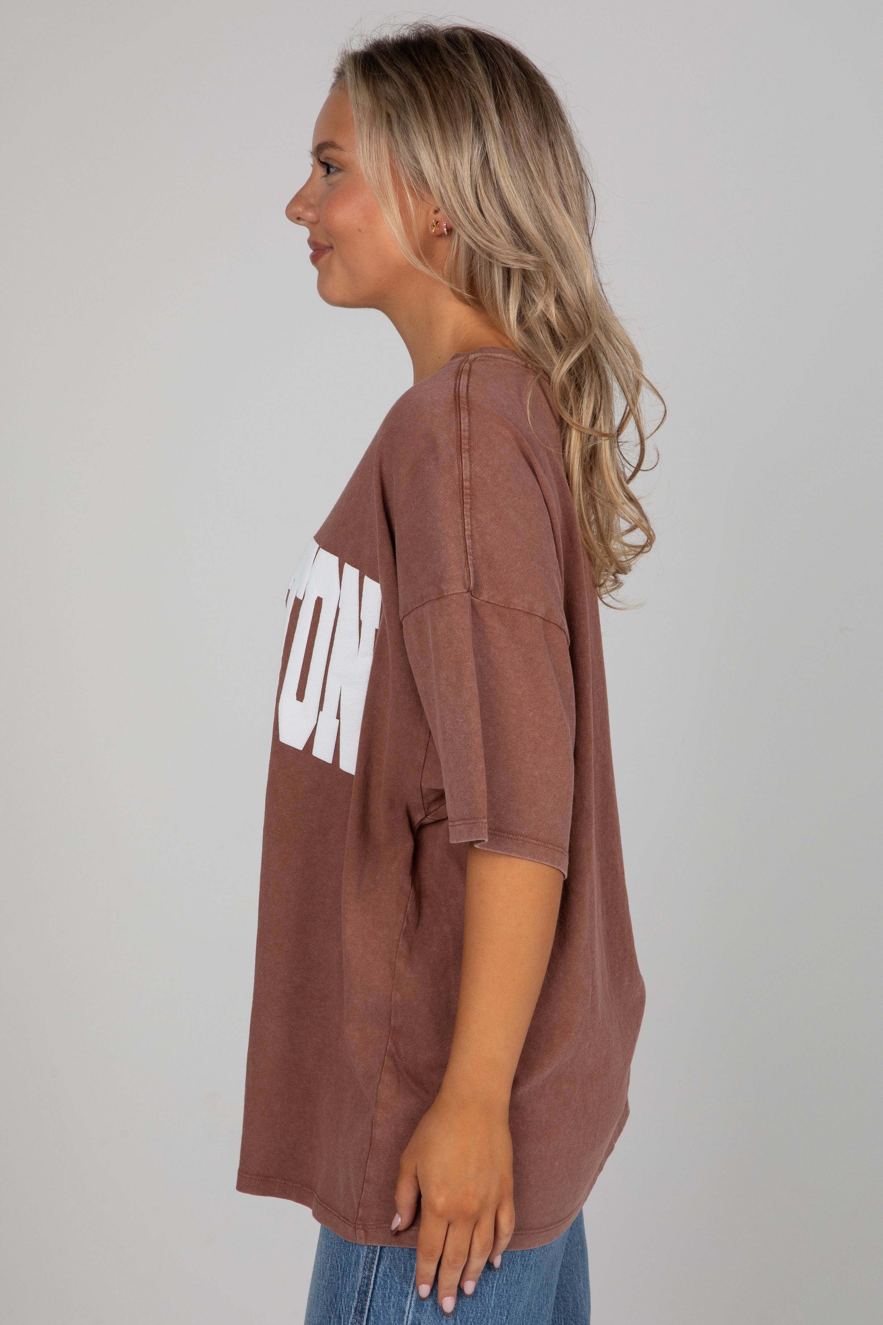 Woman wearing a brown oversized t-shirt with text on a plain background