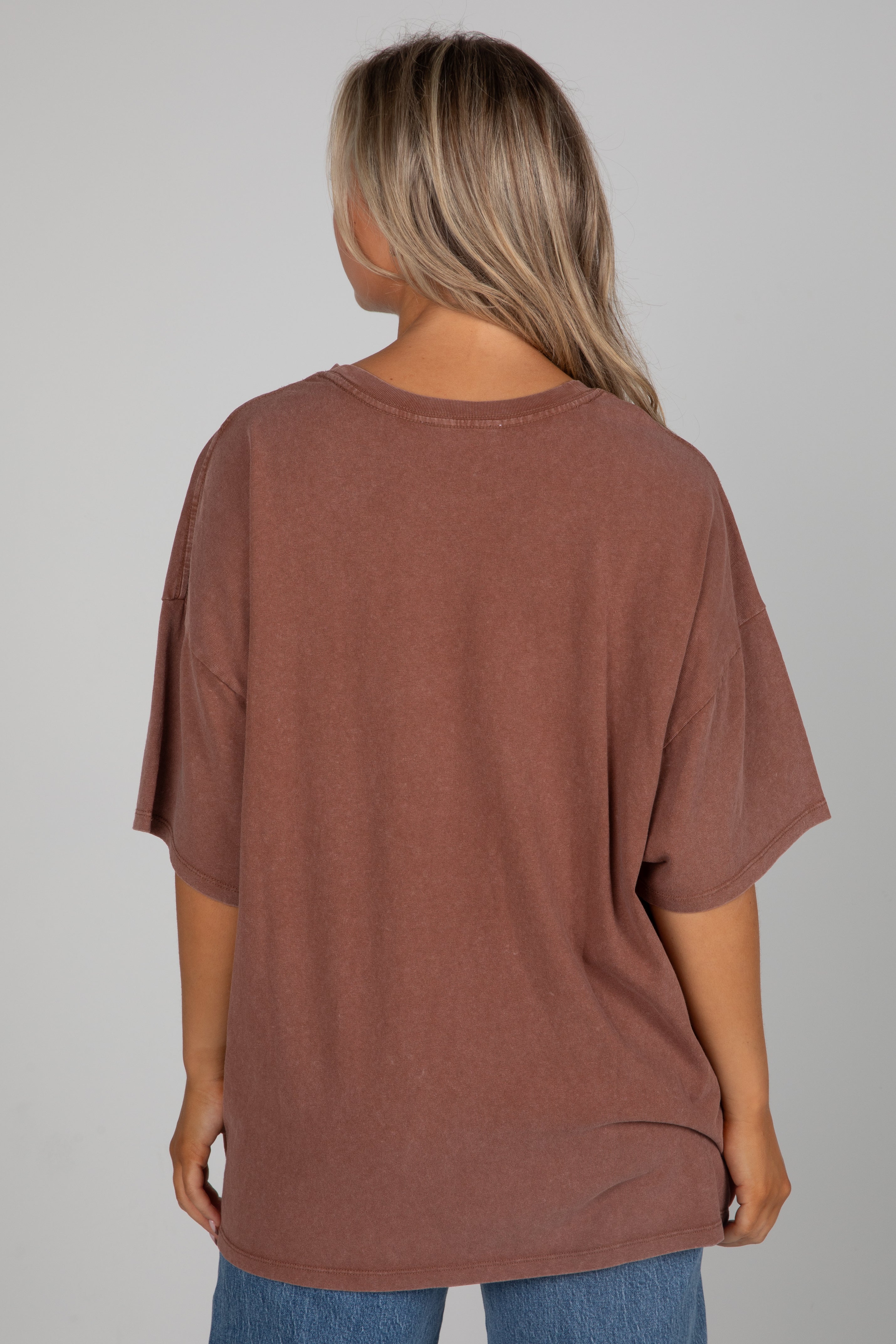 Person wearing a brown oversized t-shirt on a plain background