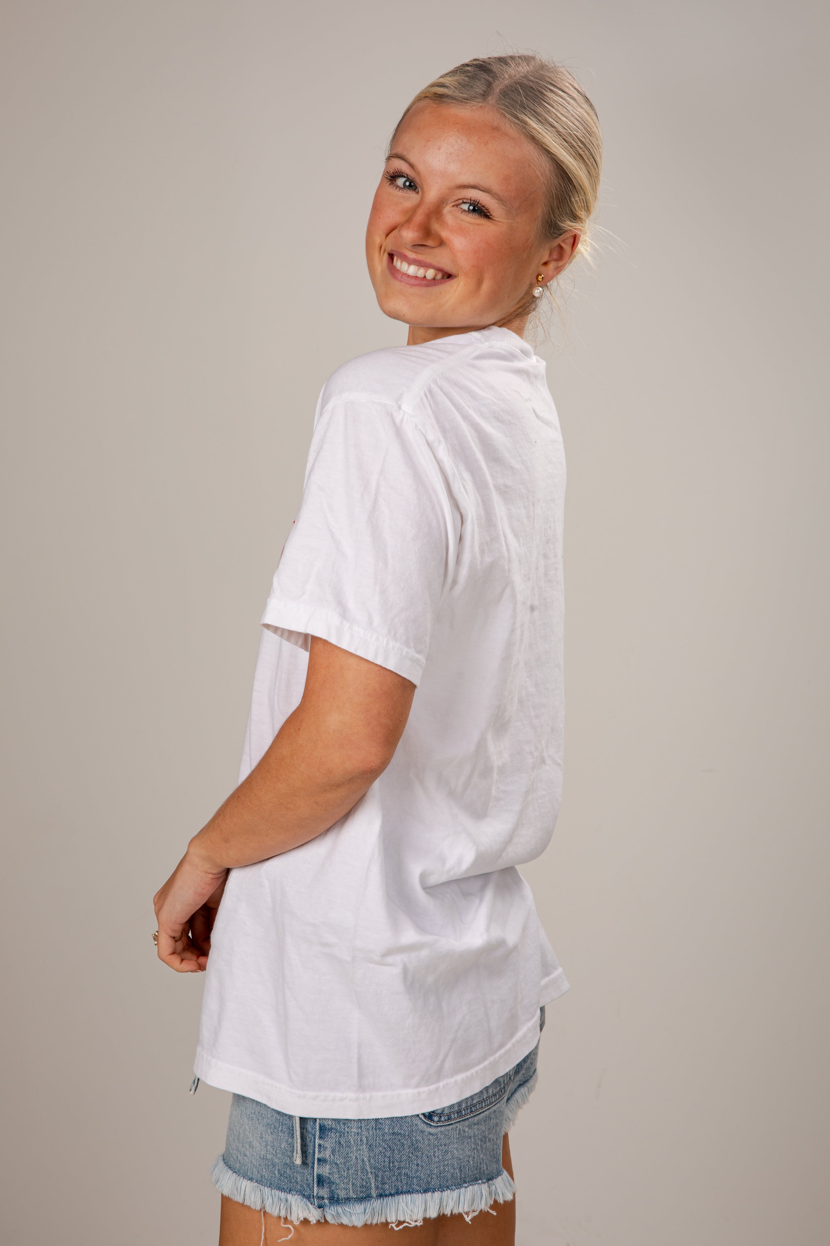 Woman wearing a white oversized shirt and denim shorts on a plain background