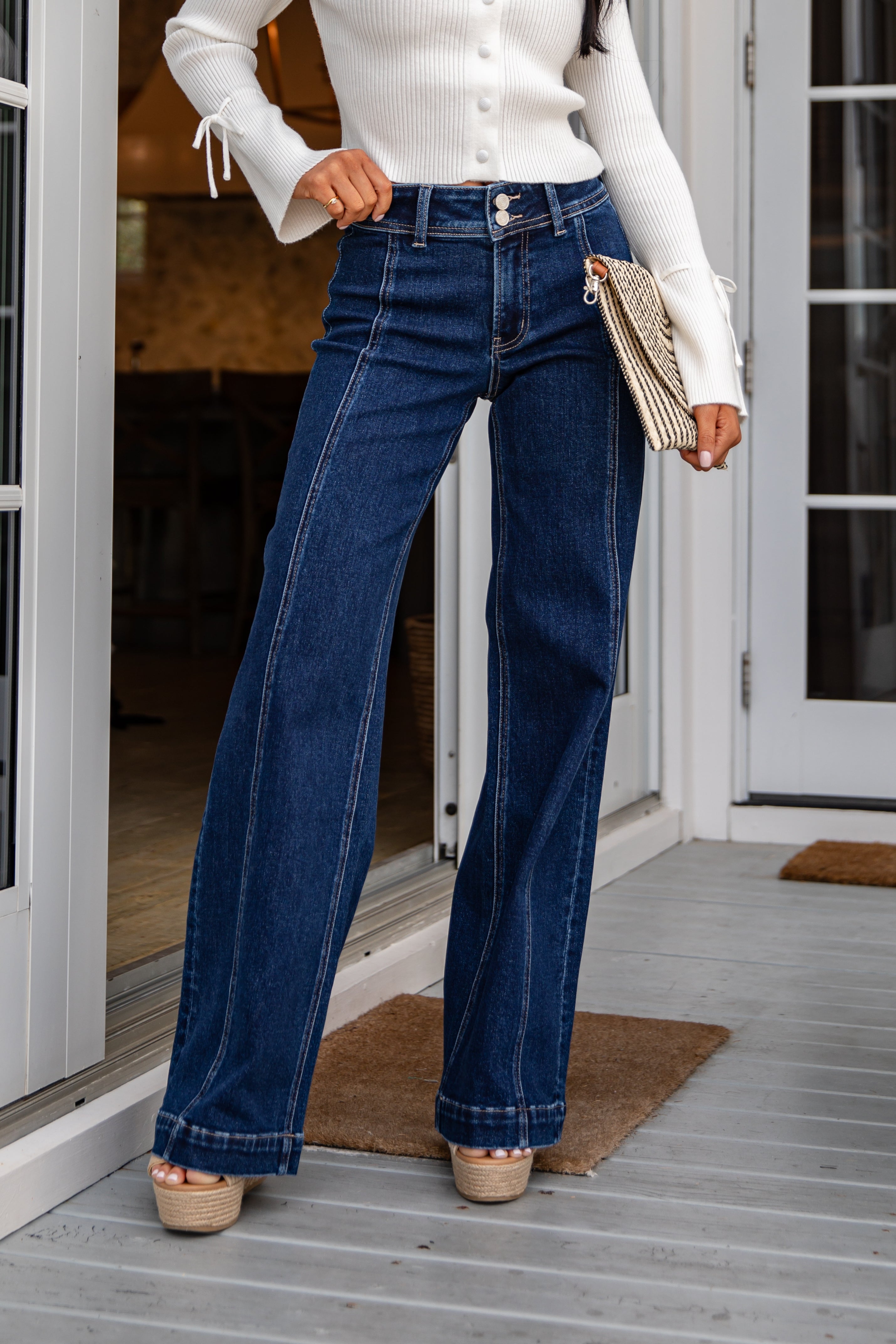 Person wearing blue jeans and a white top on a porch.