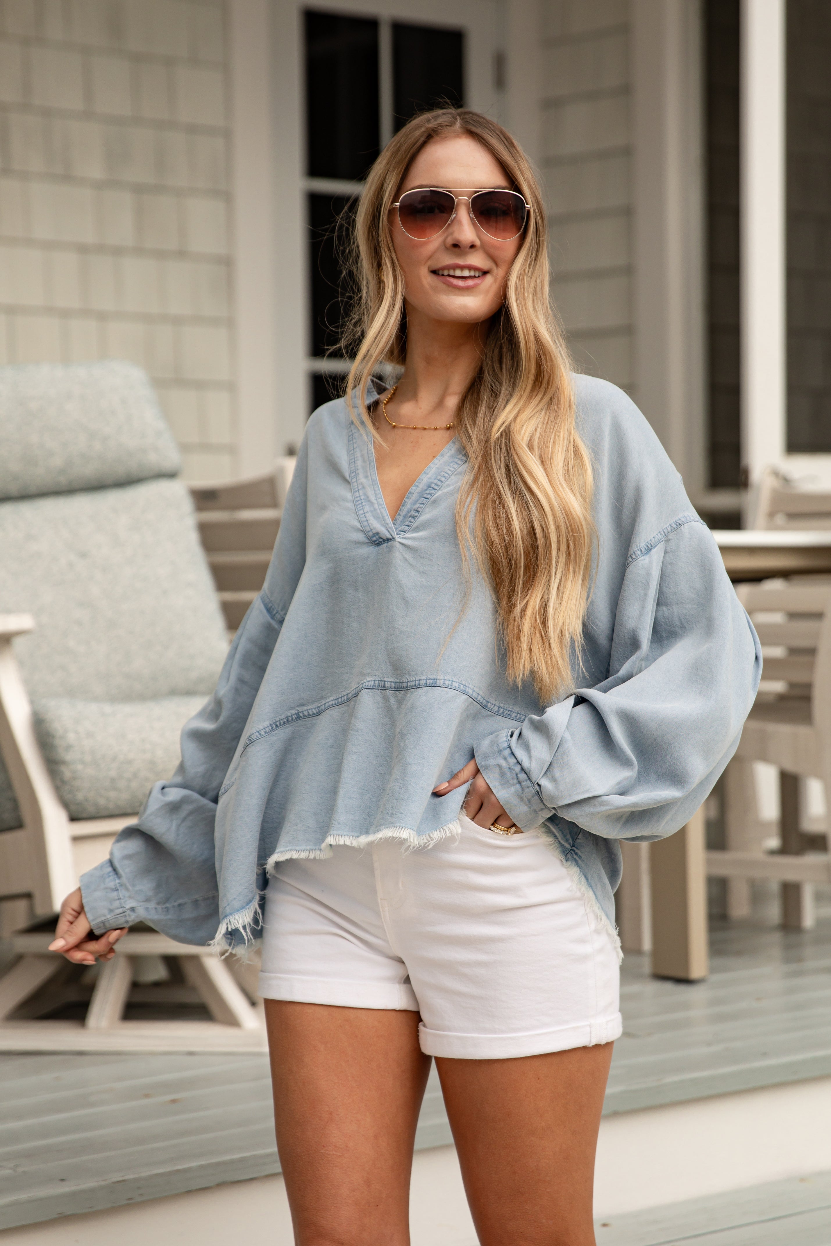 Woman wearing a light blue oversized shirt and white shorts on a porch.