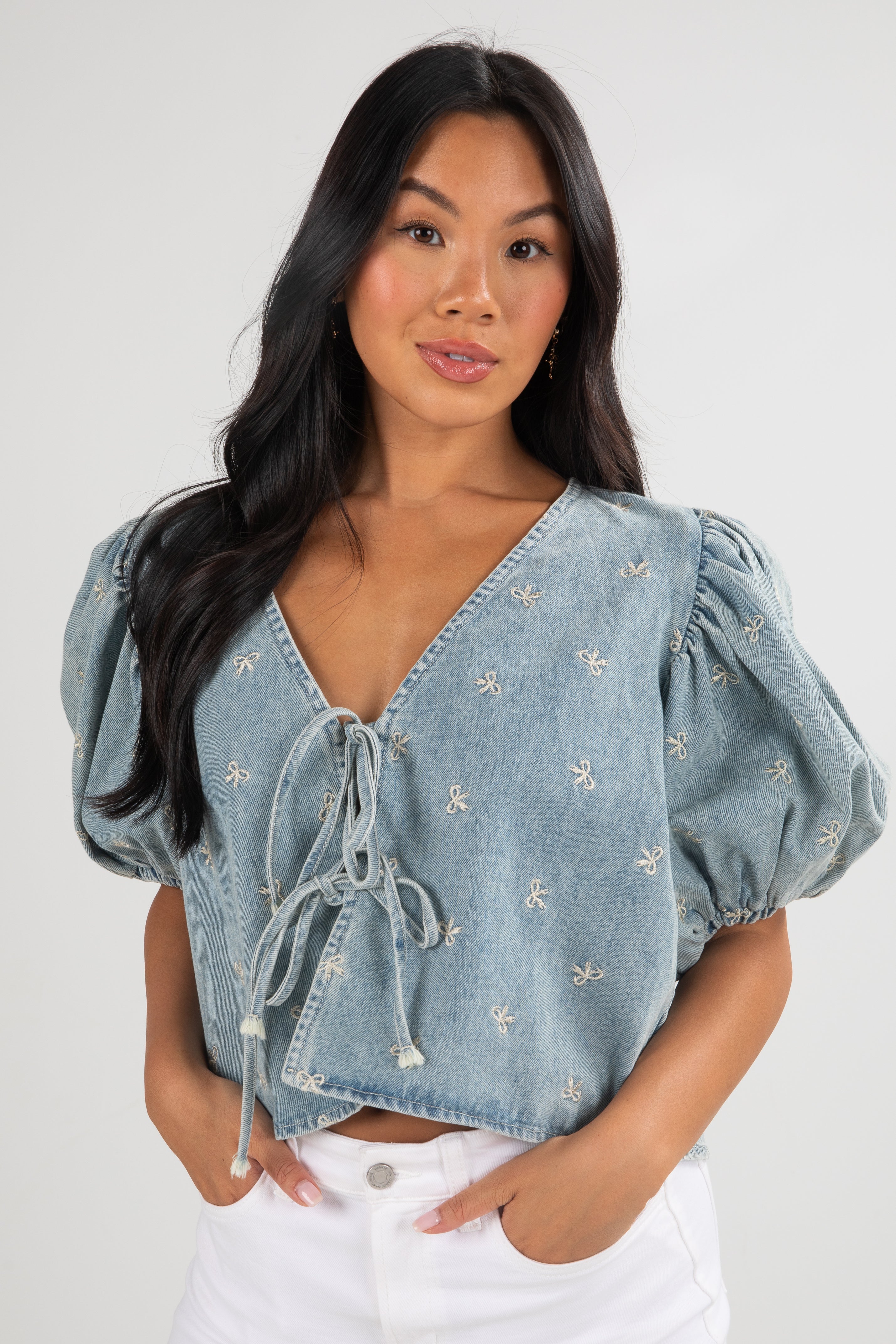 Woman wearing a light blue denim top with embroidered details on a white background