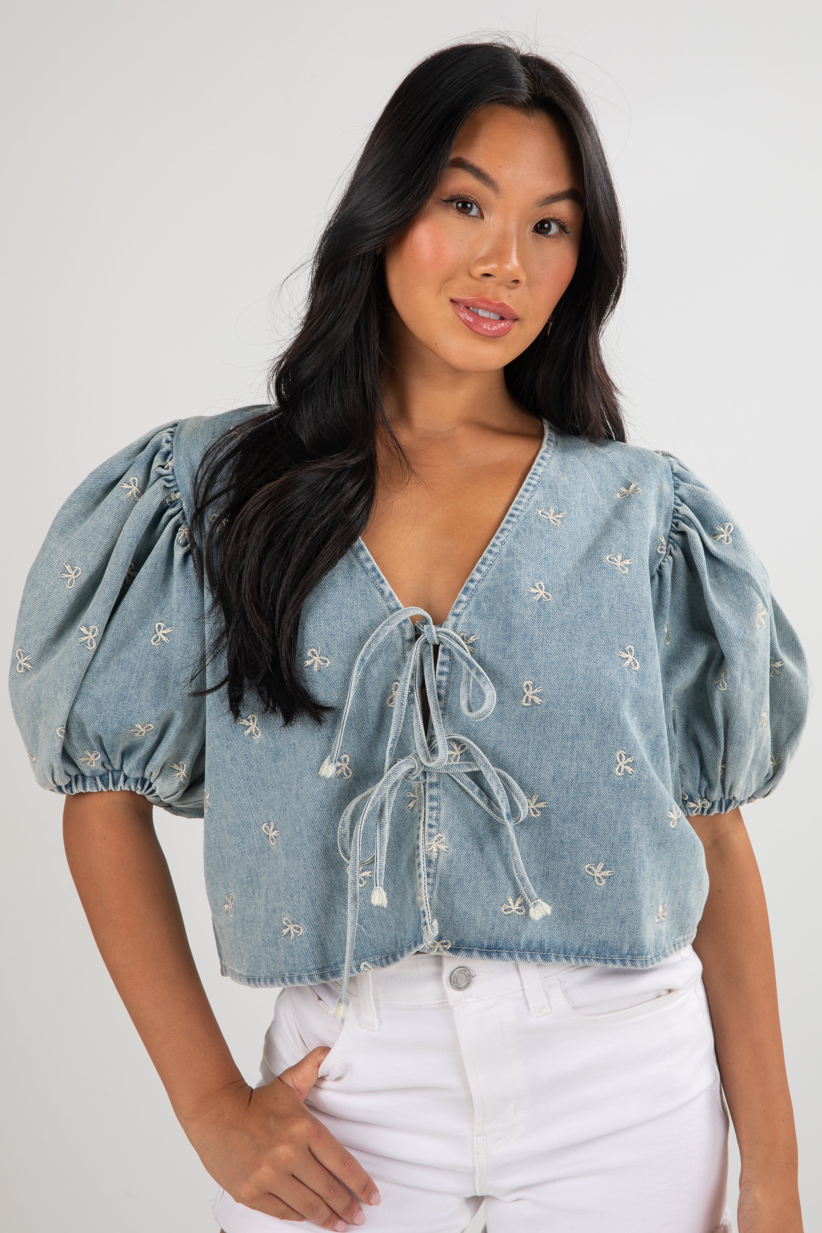 Woman wearing a light blue denim top with puff sleeves against a white background