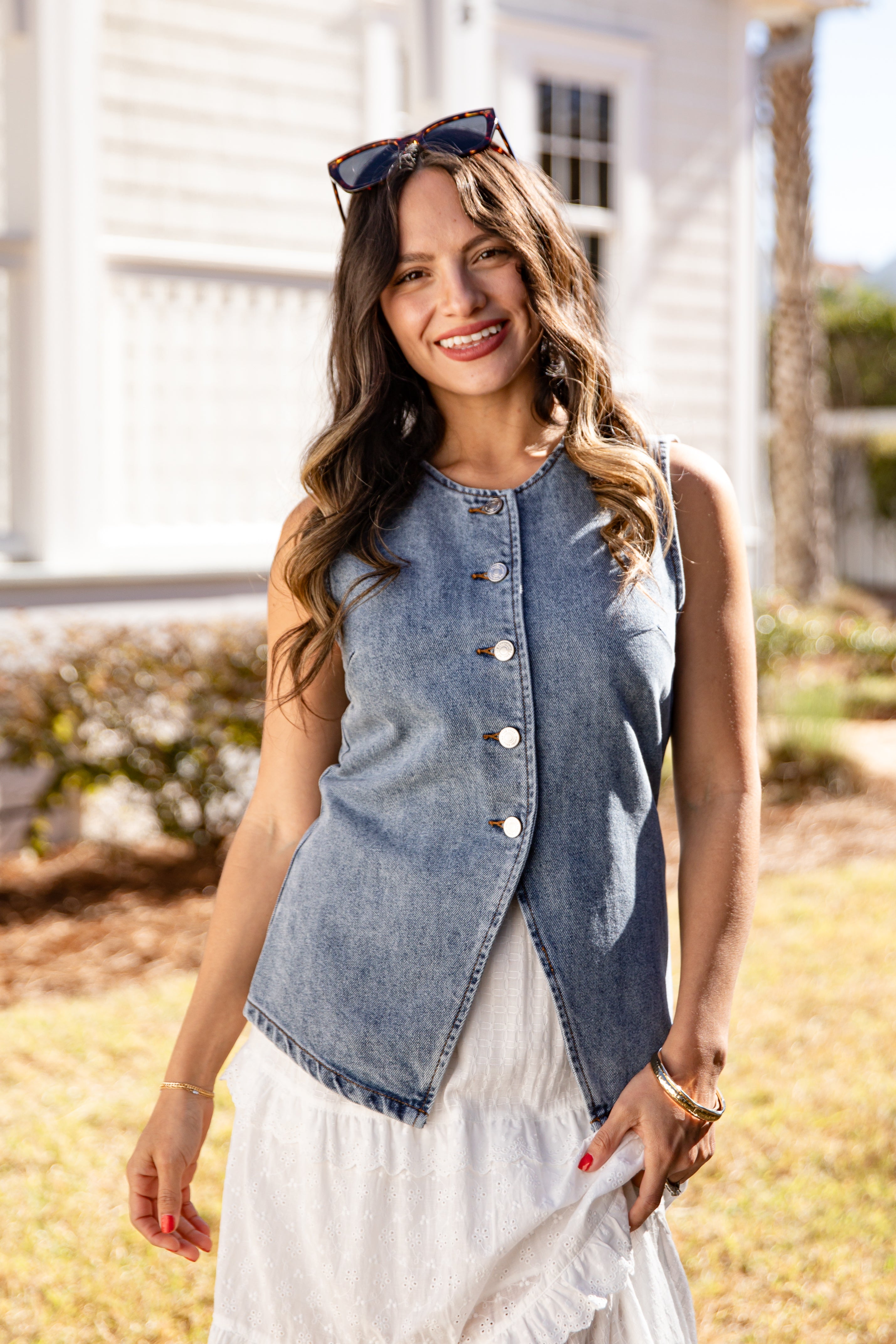 Woman wearing a denim vest over a white dress outdoors.