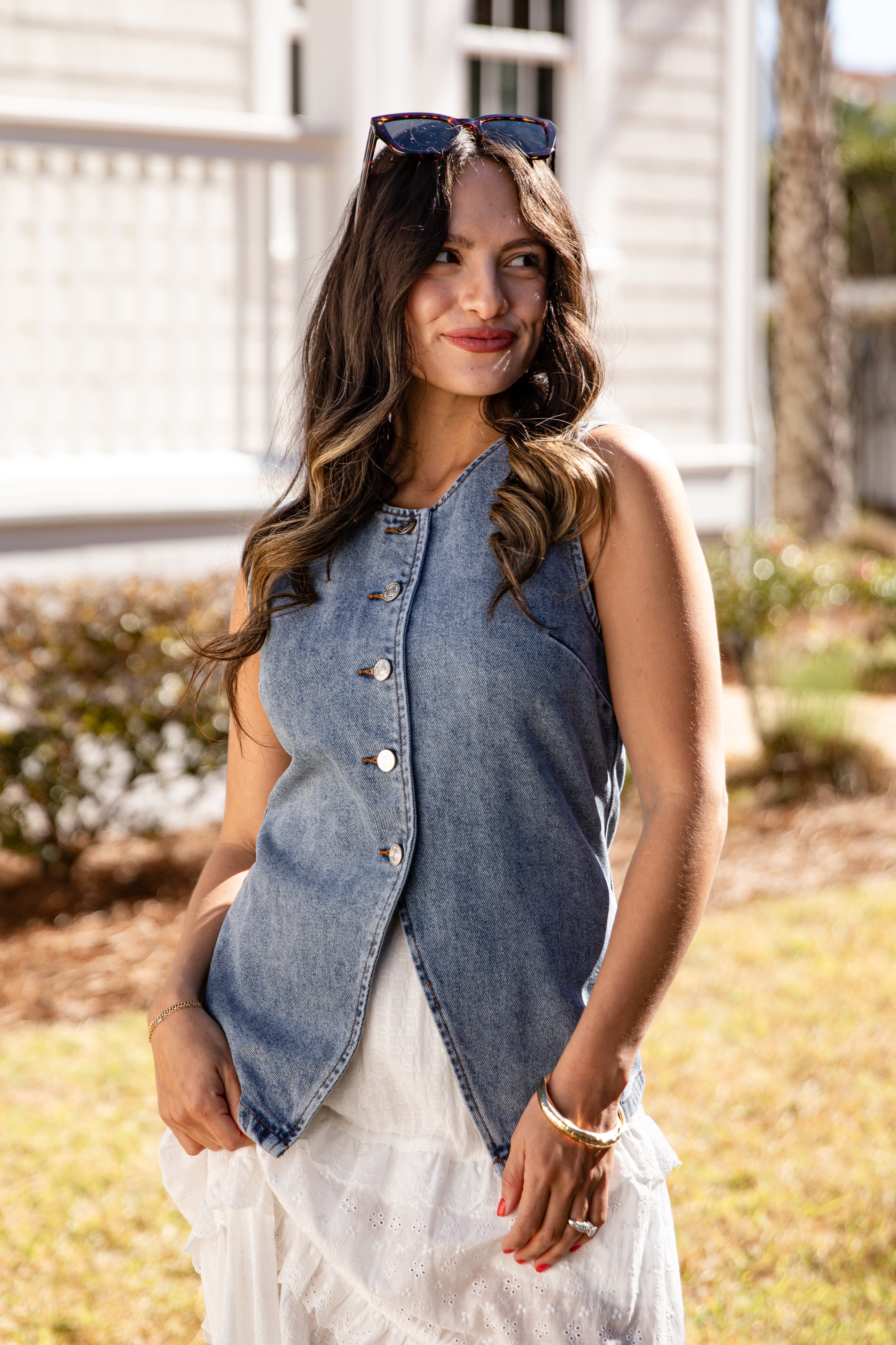 Woman wearing a denim vest over a white dress outdoors.