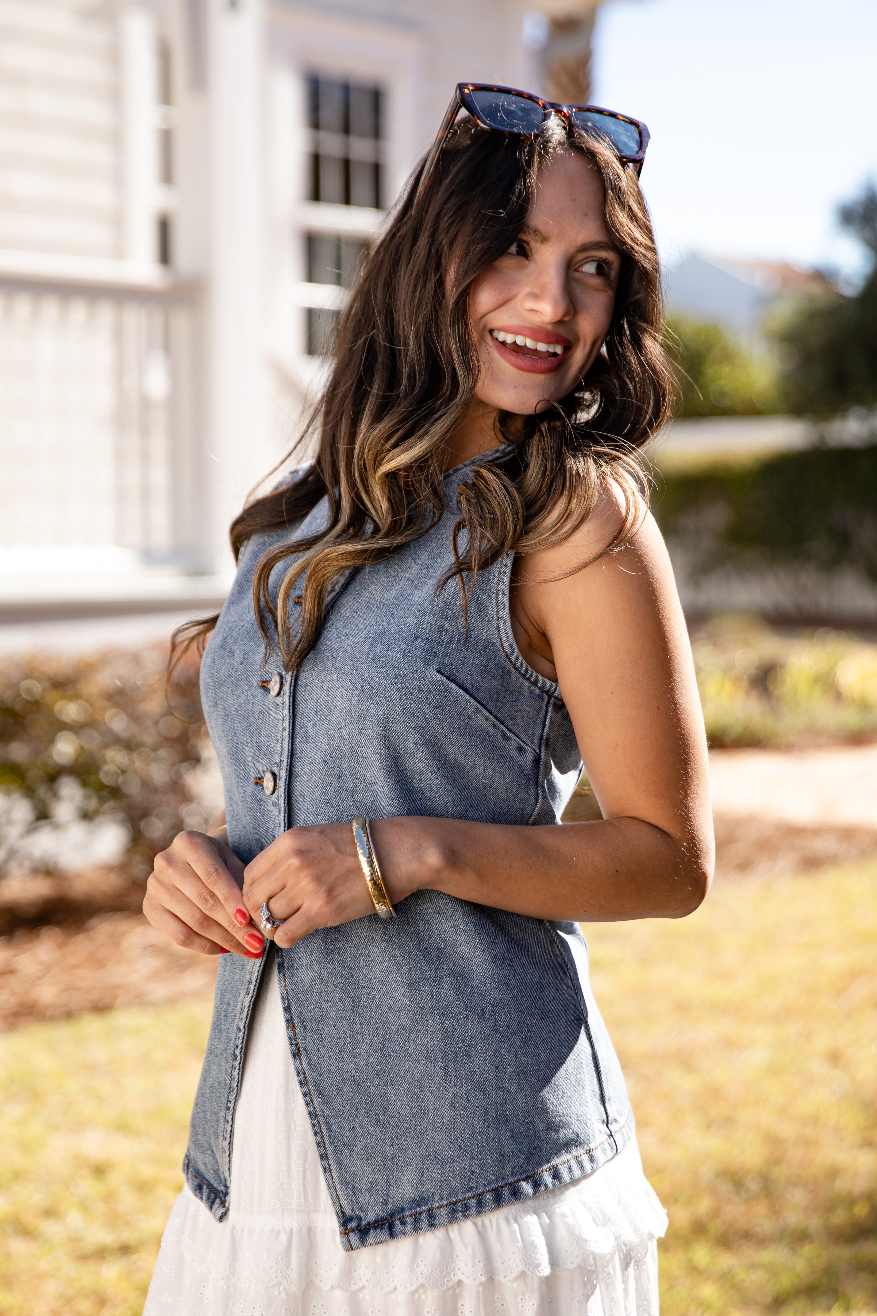 Woman wearing a denim vest over a white dress outdoors