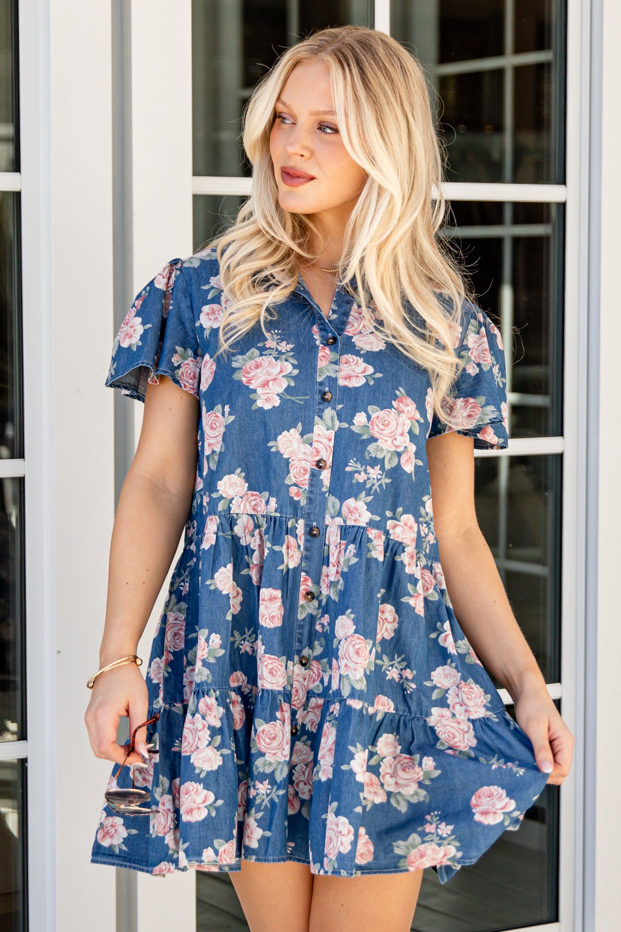 Woman wearing a blue floral dress standing in front of glass doors.