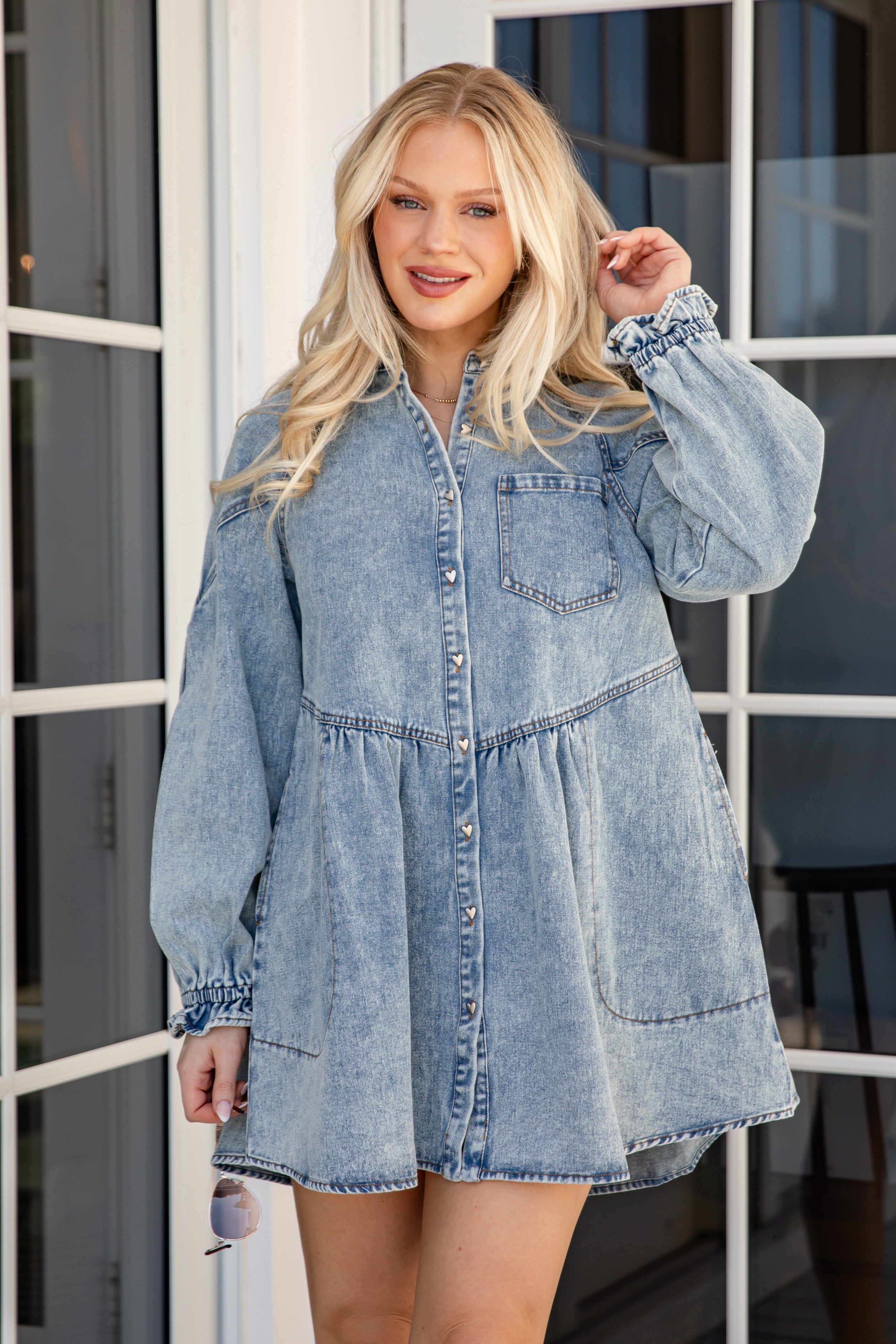 Woman wearing a denim dress standing in front of a glass door.