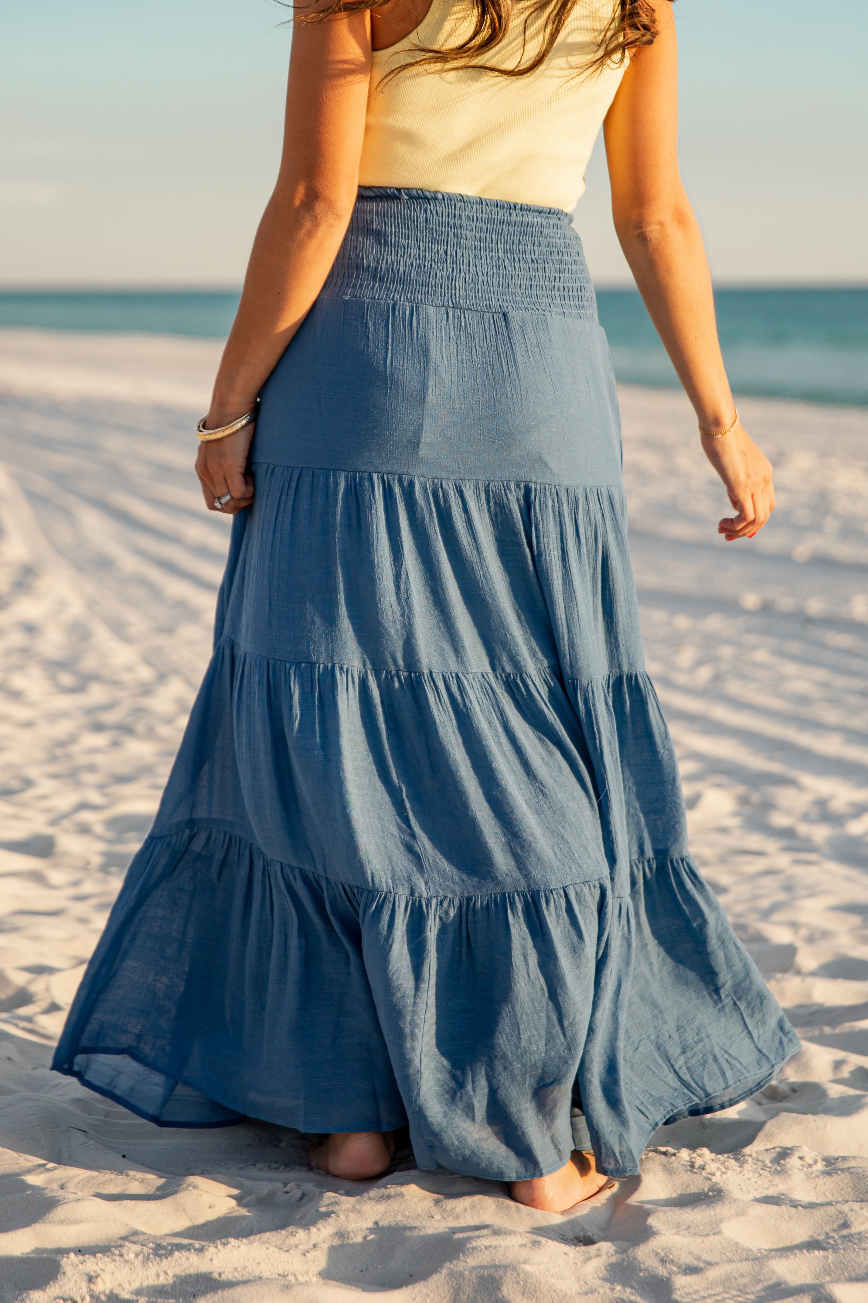 Woman wearing a blue tiered skirt on a sandy beach with ocean view