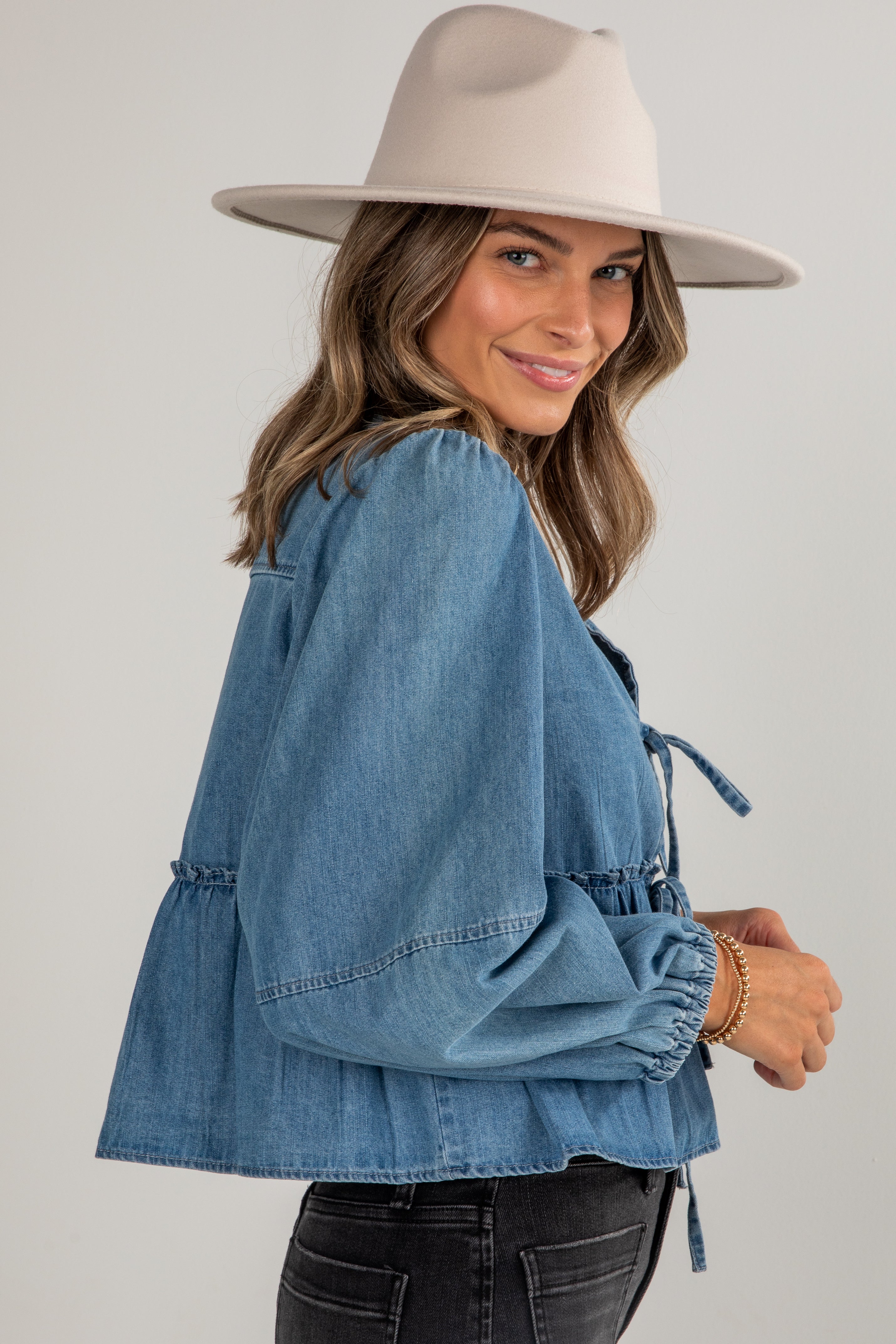 Woman wearing a denim jacket and beige hat on a plain background