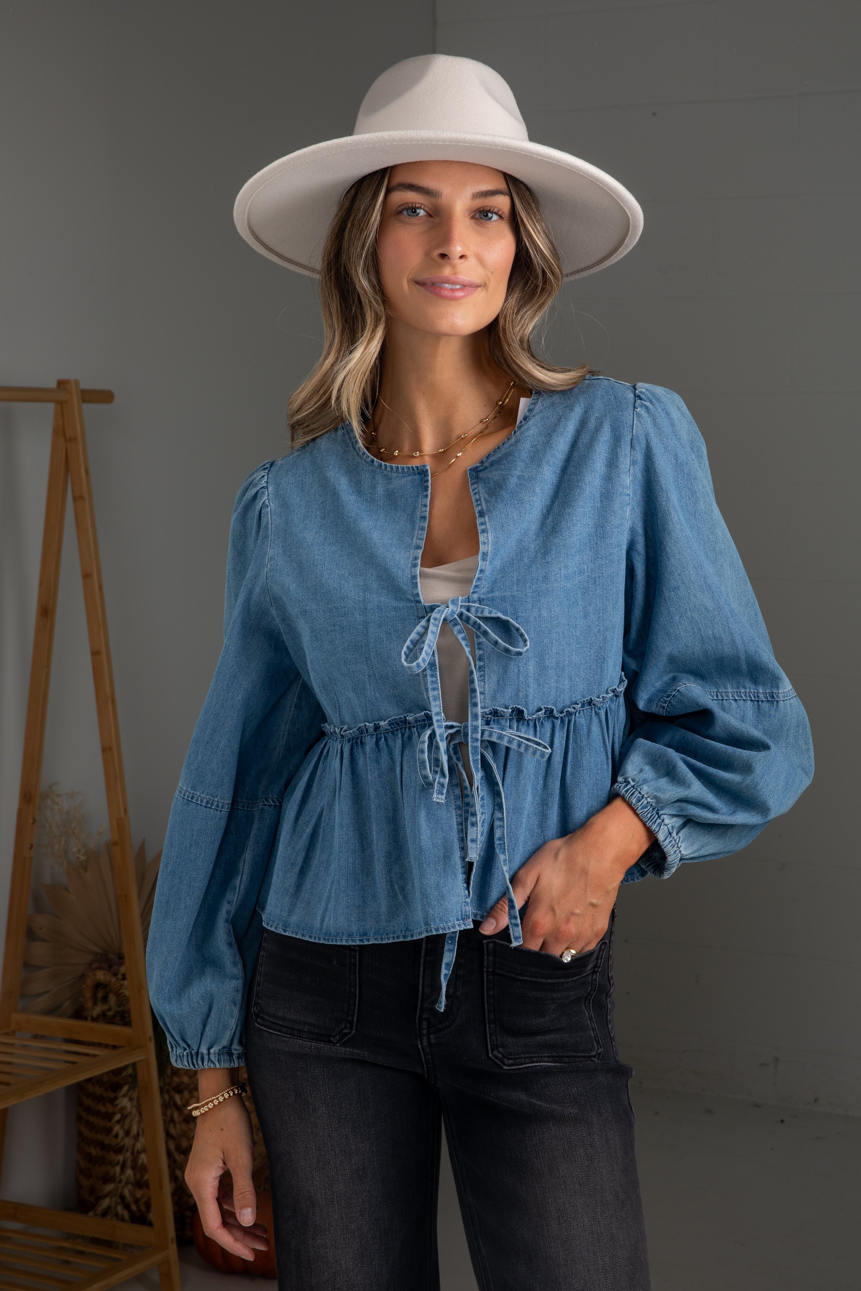 Woman wearing a blue denim blouse and white hat against a gray background