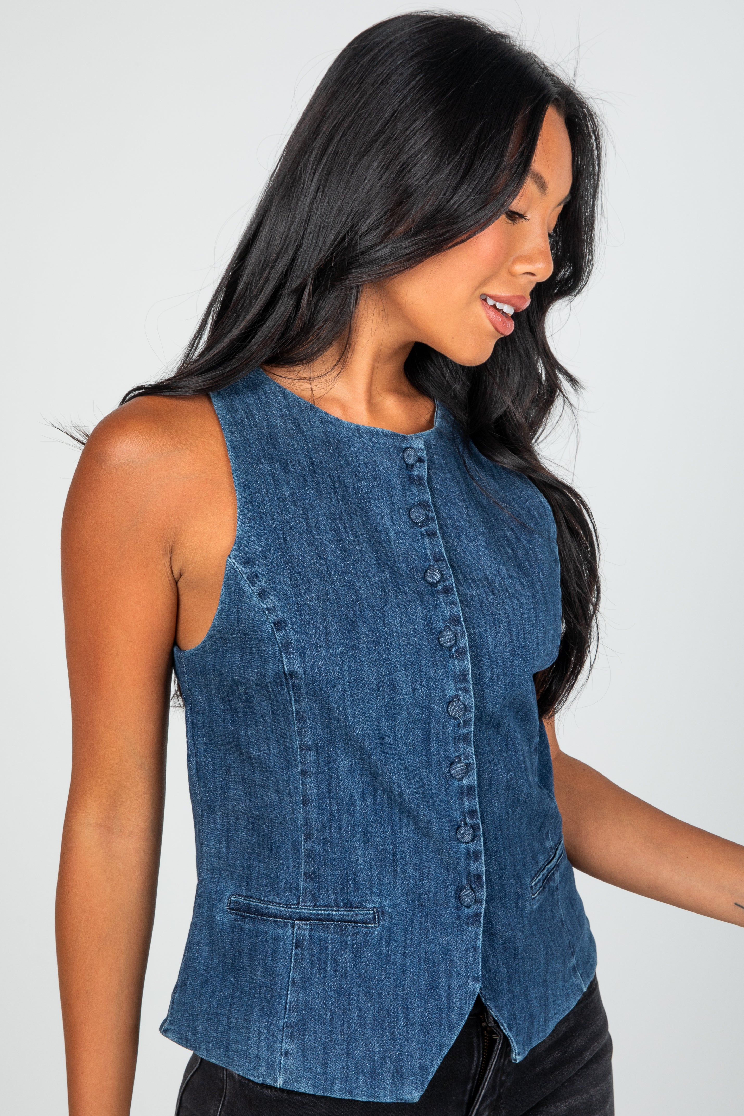 Woman wearing a blue denim sleeveless top against a plain background