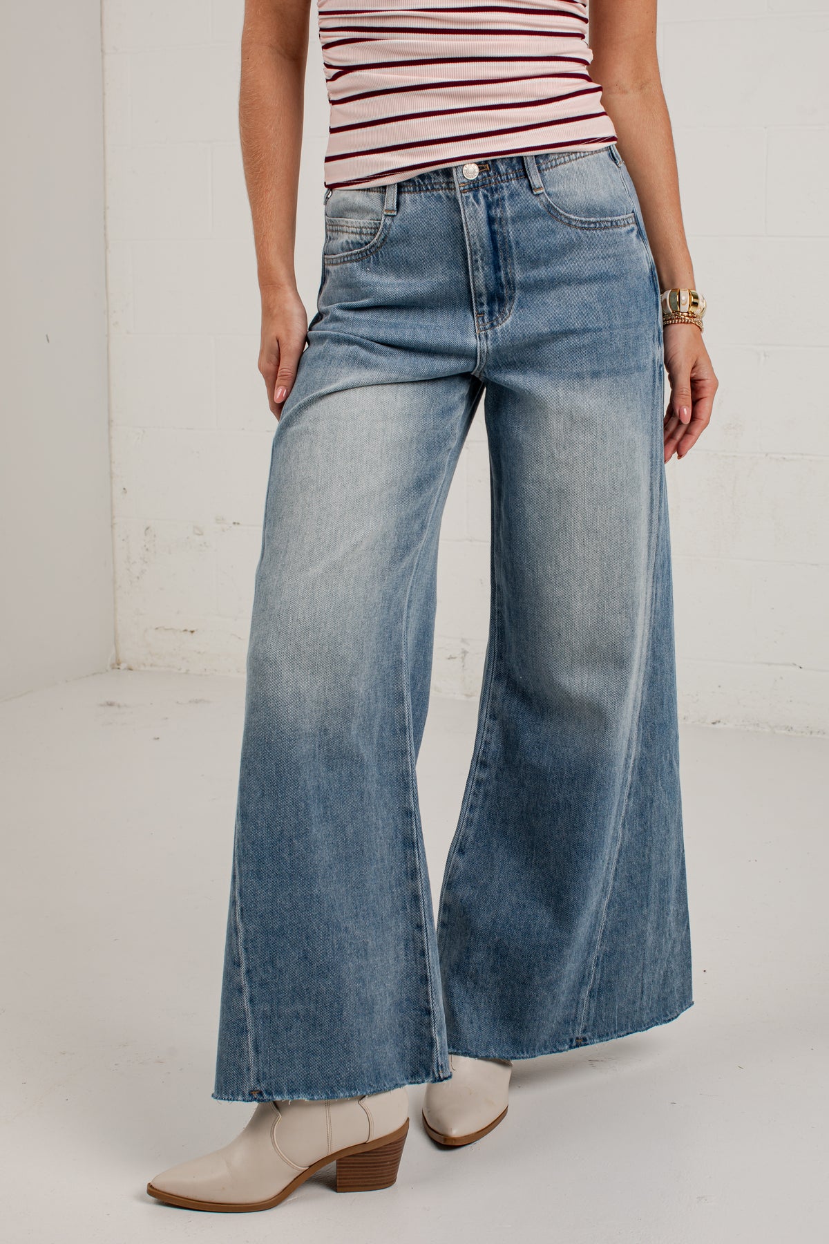 A model wearing a pair of wide-leg, light-wash blue denim jeans with a faded wash, paired with a red and white striped top and beige ankle boots.