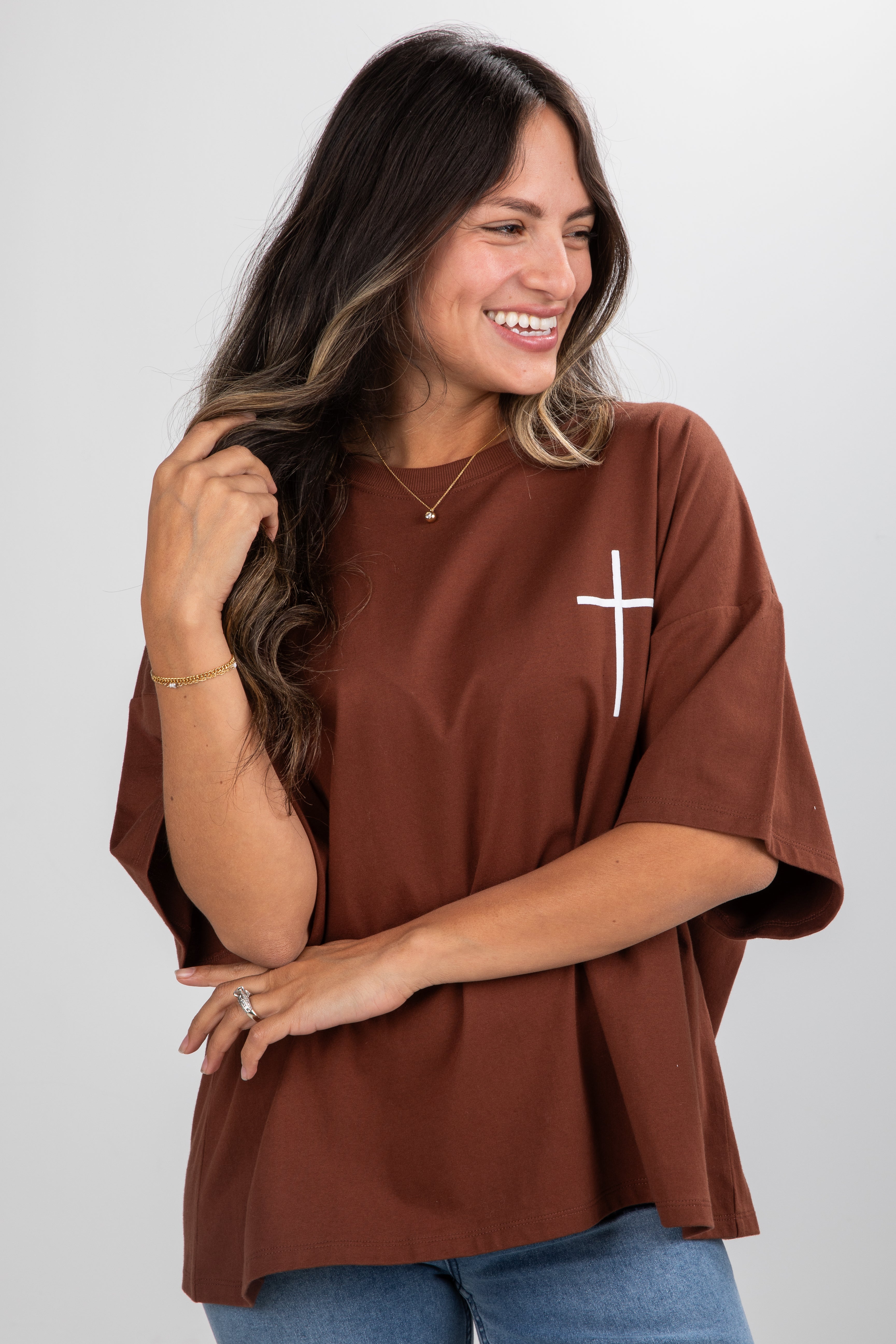 Woman wearing a brown t-shirt with a white cross design on a plain background