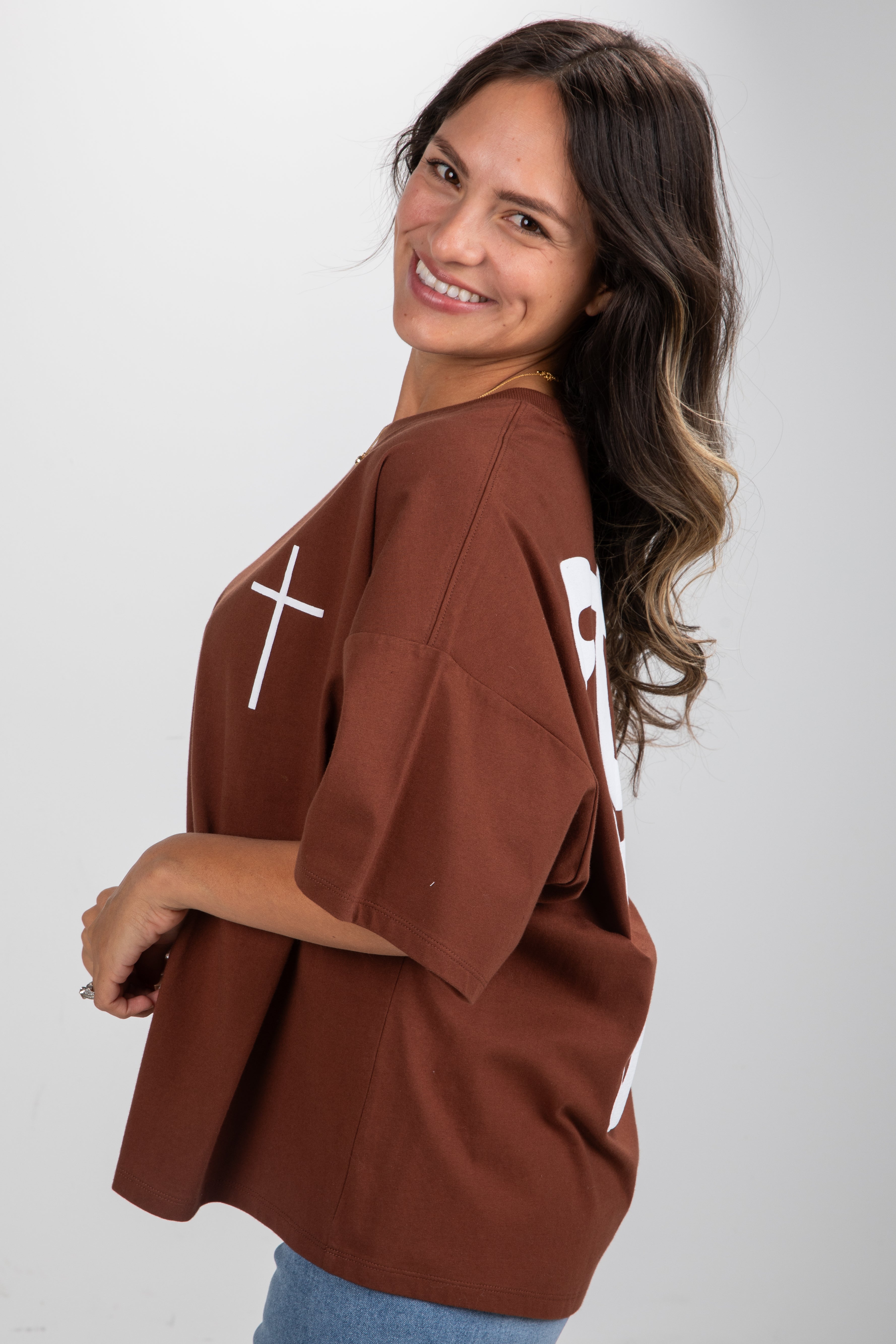 Woman wearing a brown oversized shirt with white designs on a plain background