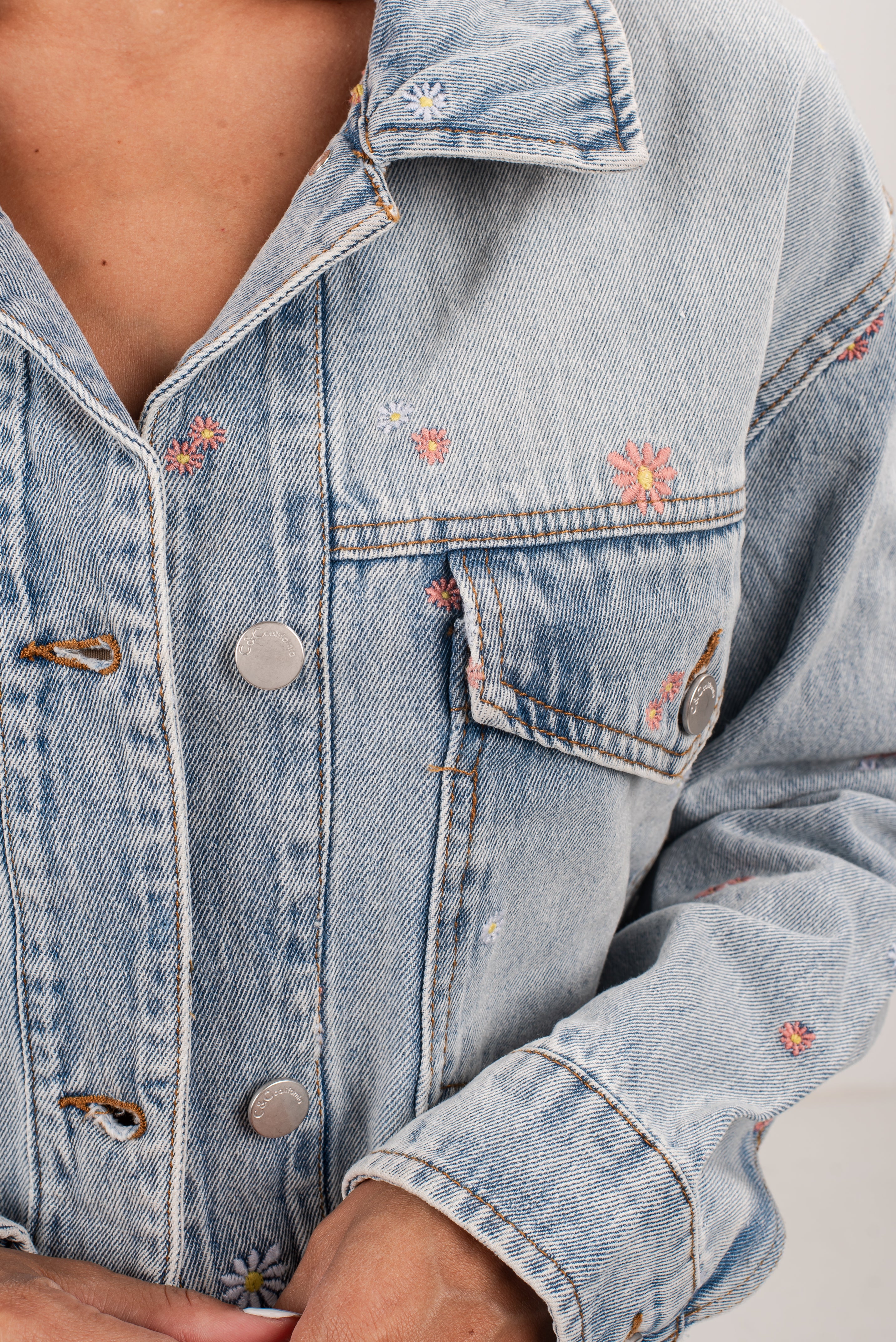 Light blue denim jacket with floral embroidery on a neutral background