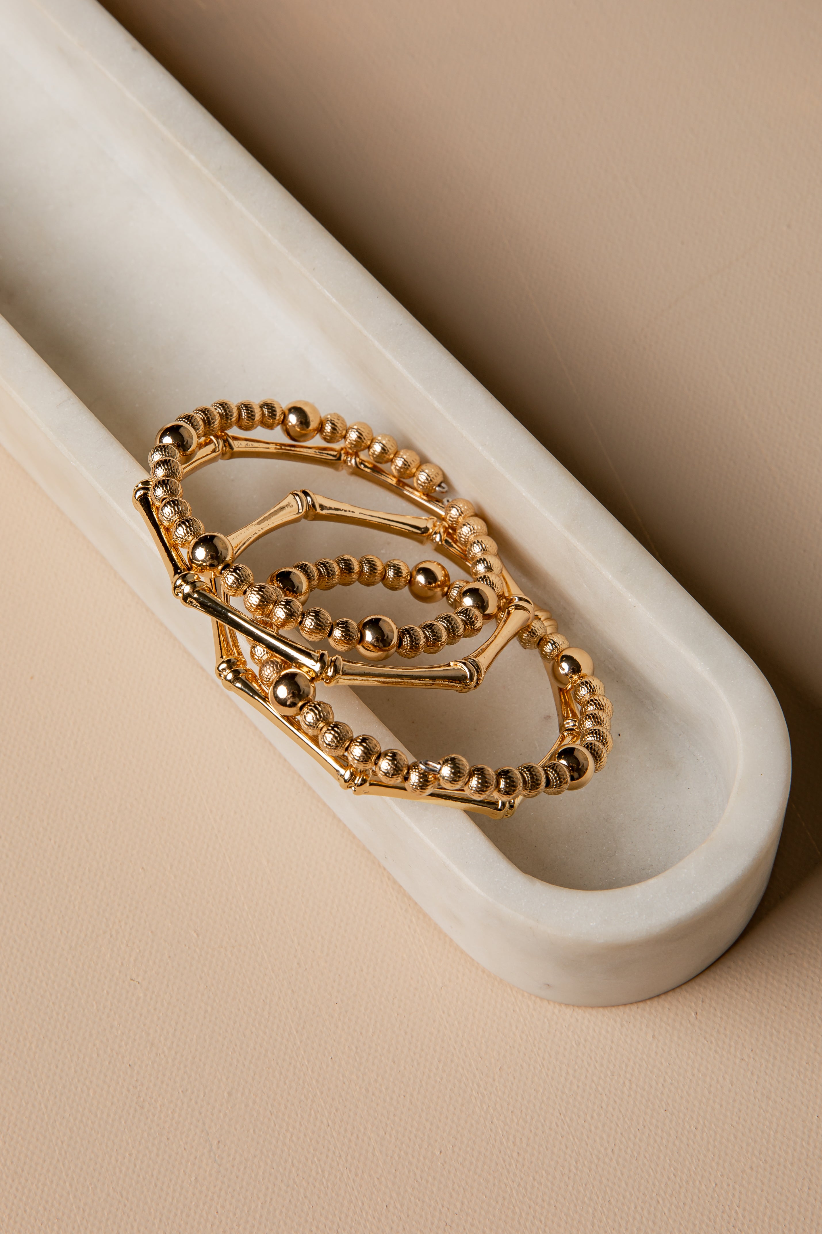 Three gold rings stacked on a white marble surface with a beige background