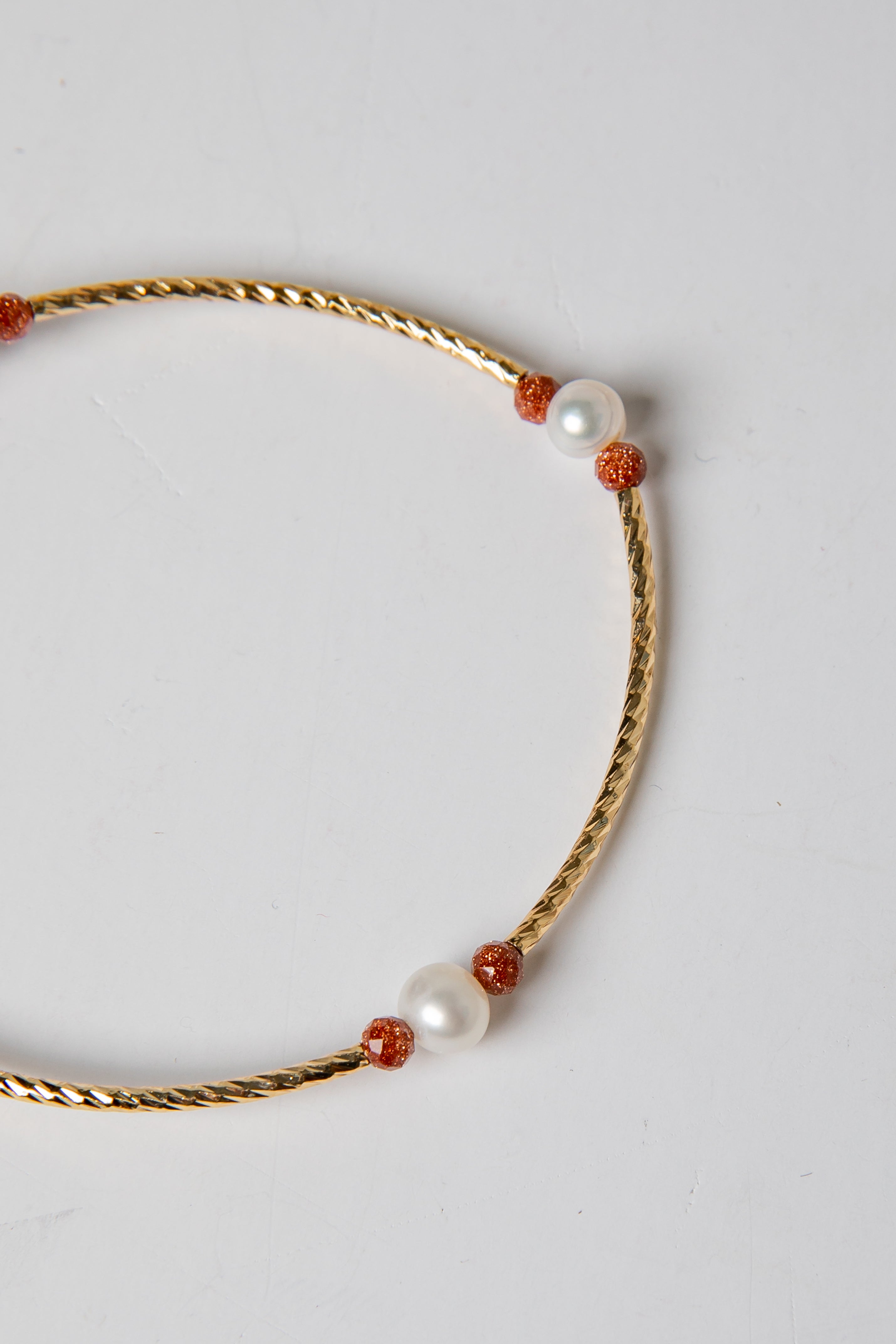 Gold necklace with pearls and red beads on a light gray background