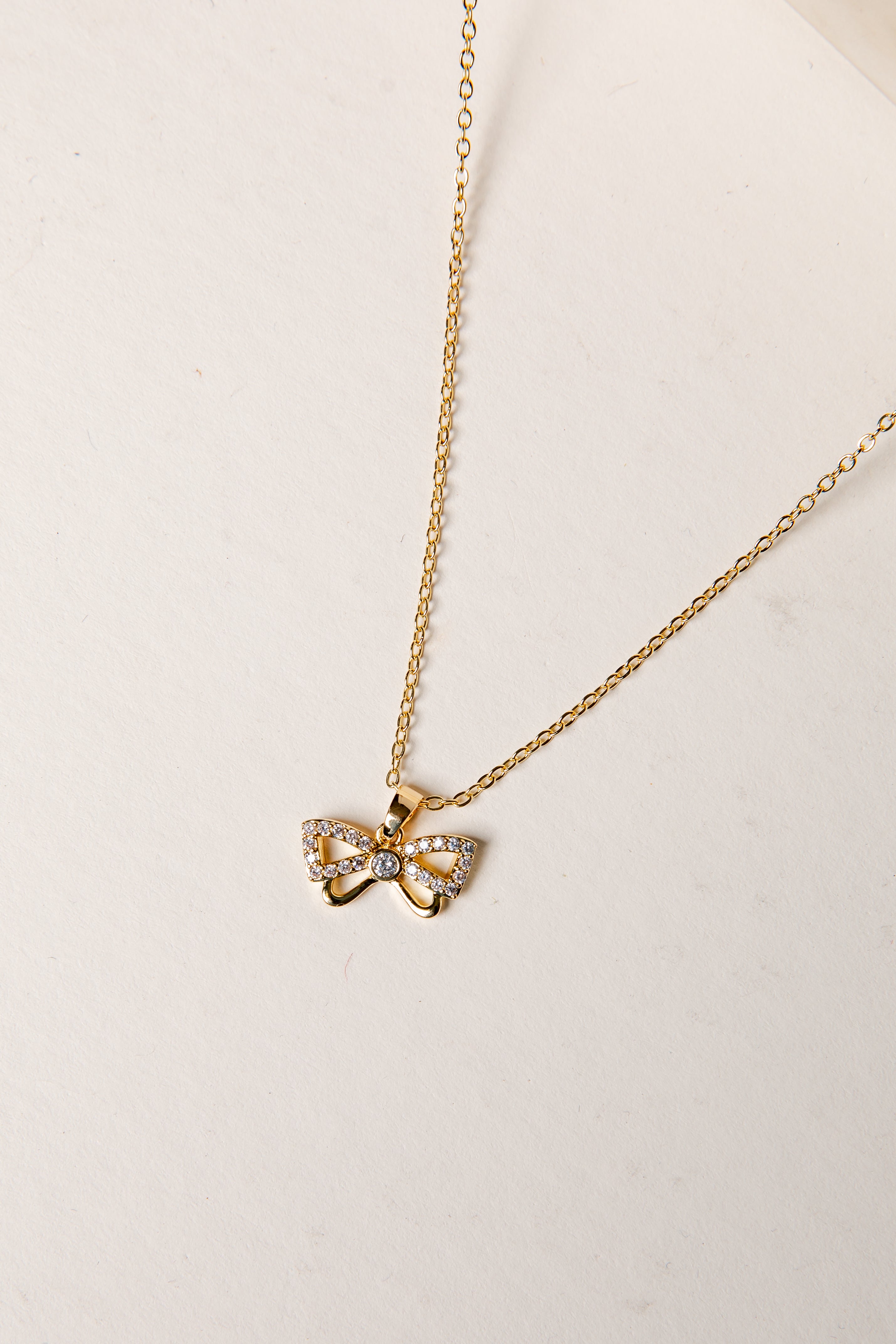 Gold necklace with a bow-shaped pendant on a light background