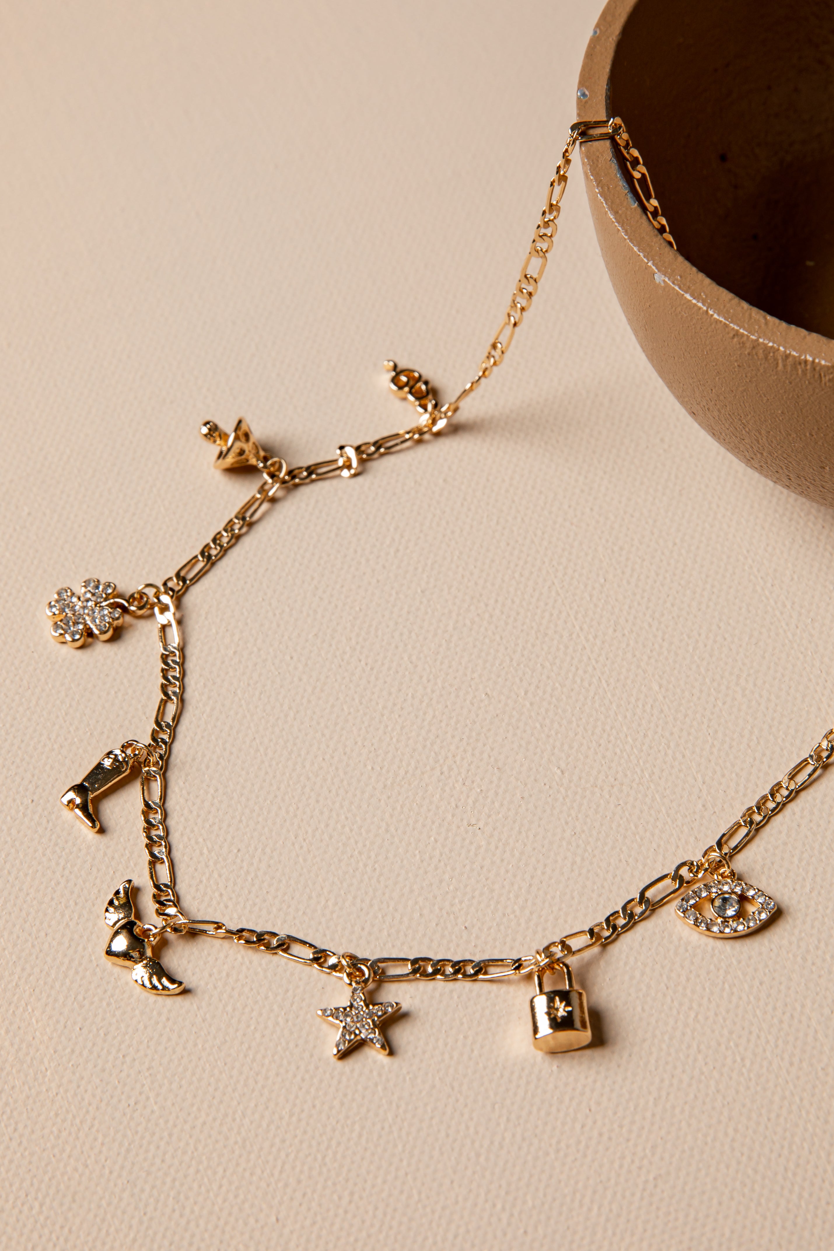 Gold bracelet with various charms on a beige surface