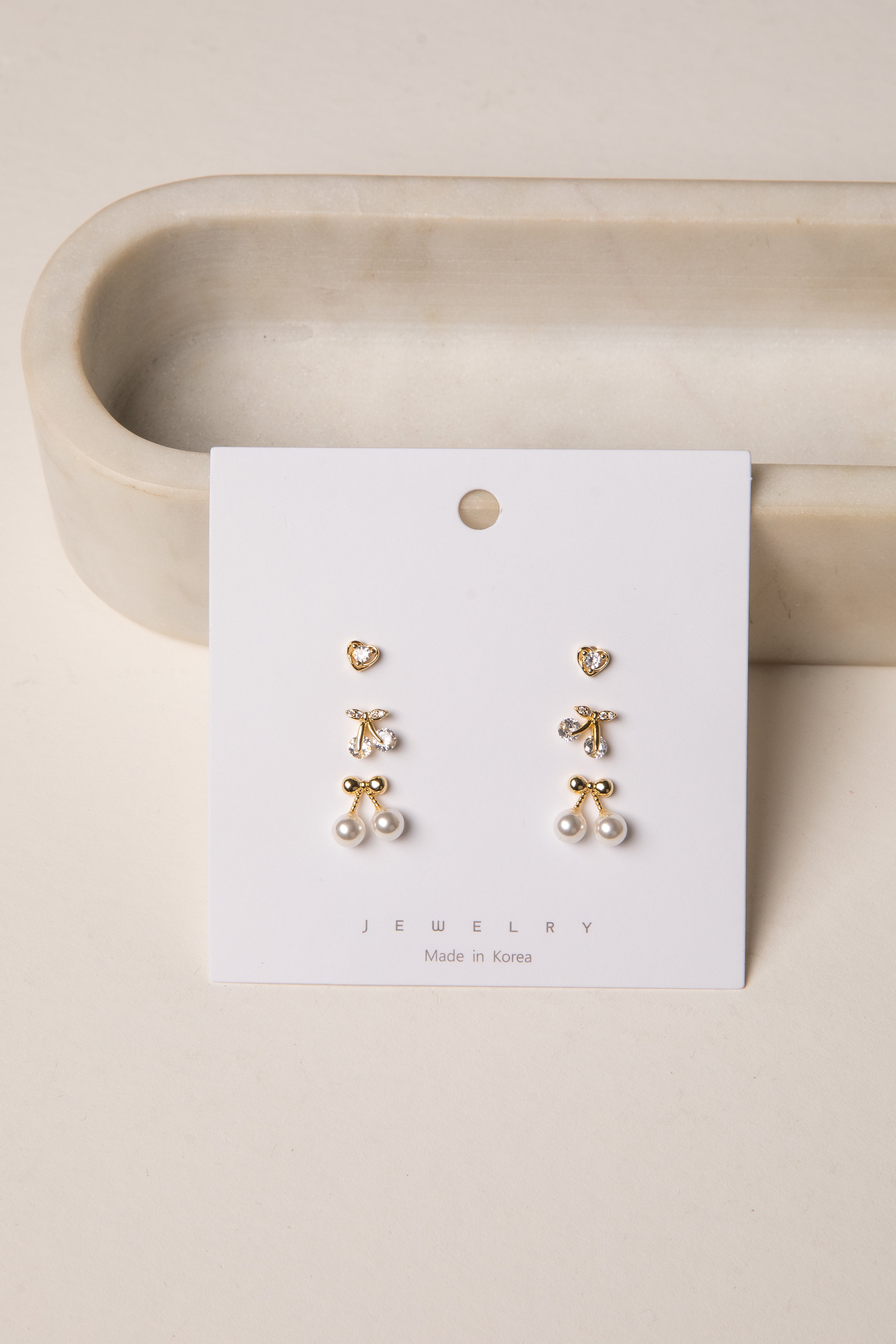 Set of gold and pearl earrings on a jewelry card with a beige background