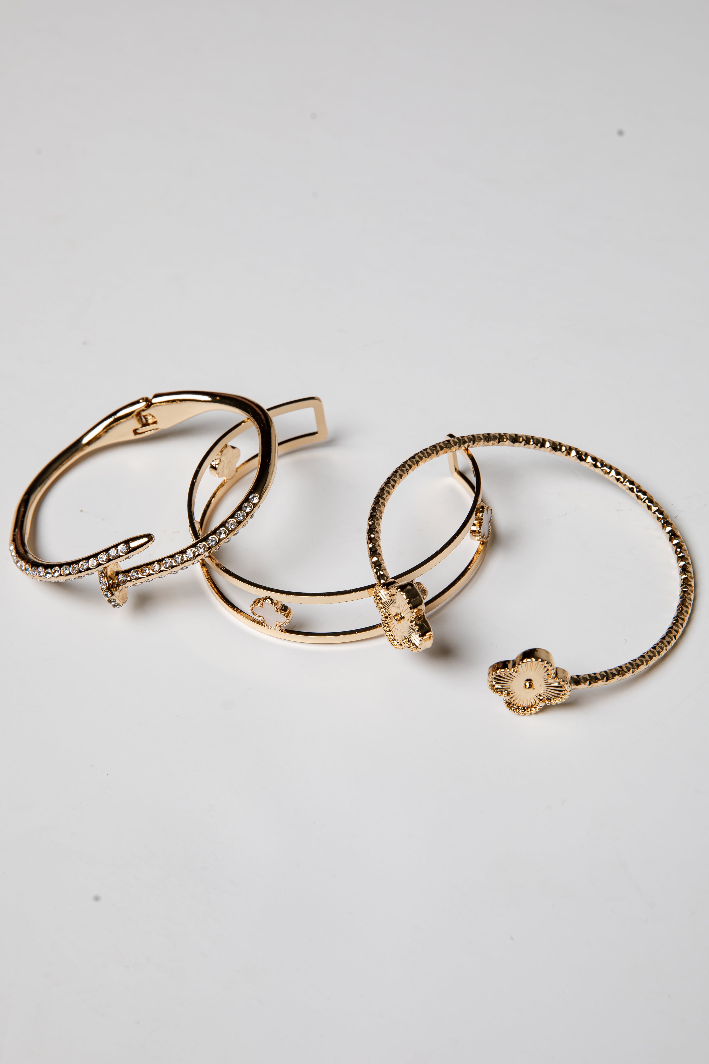 Three gold bracelets with intricate designs on a light gray background