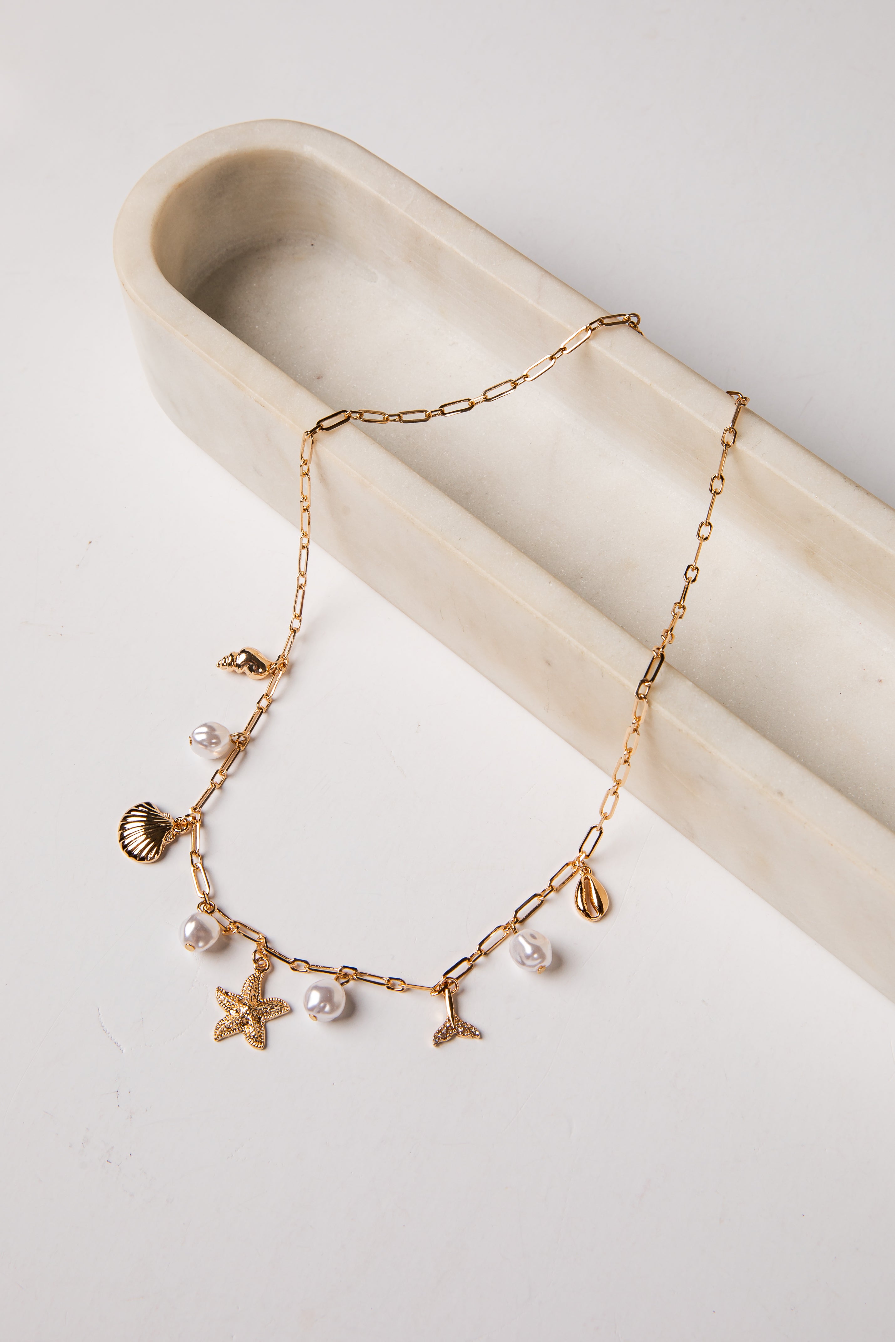 Gold necklace with starfish, shell, and pearl charms on a white surface.