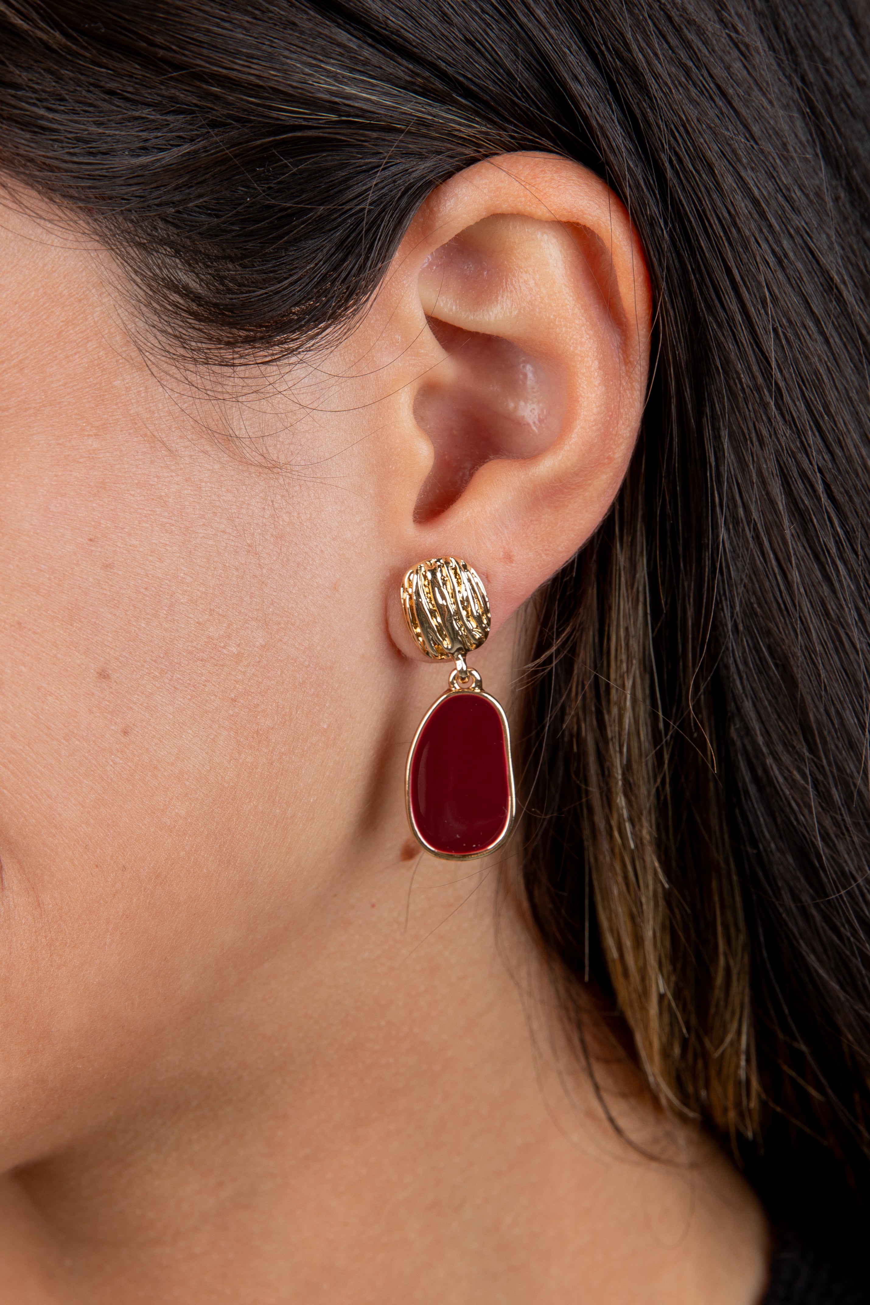 Close-up of an ear wearing a gold and red earring with dark hair.