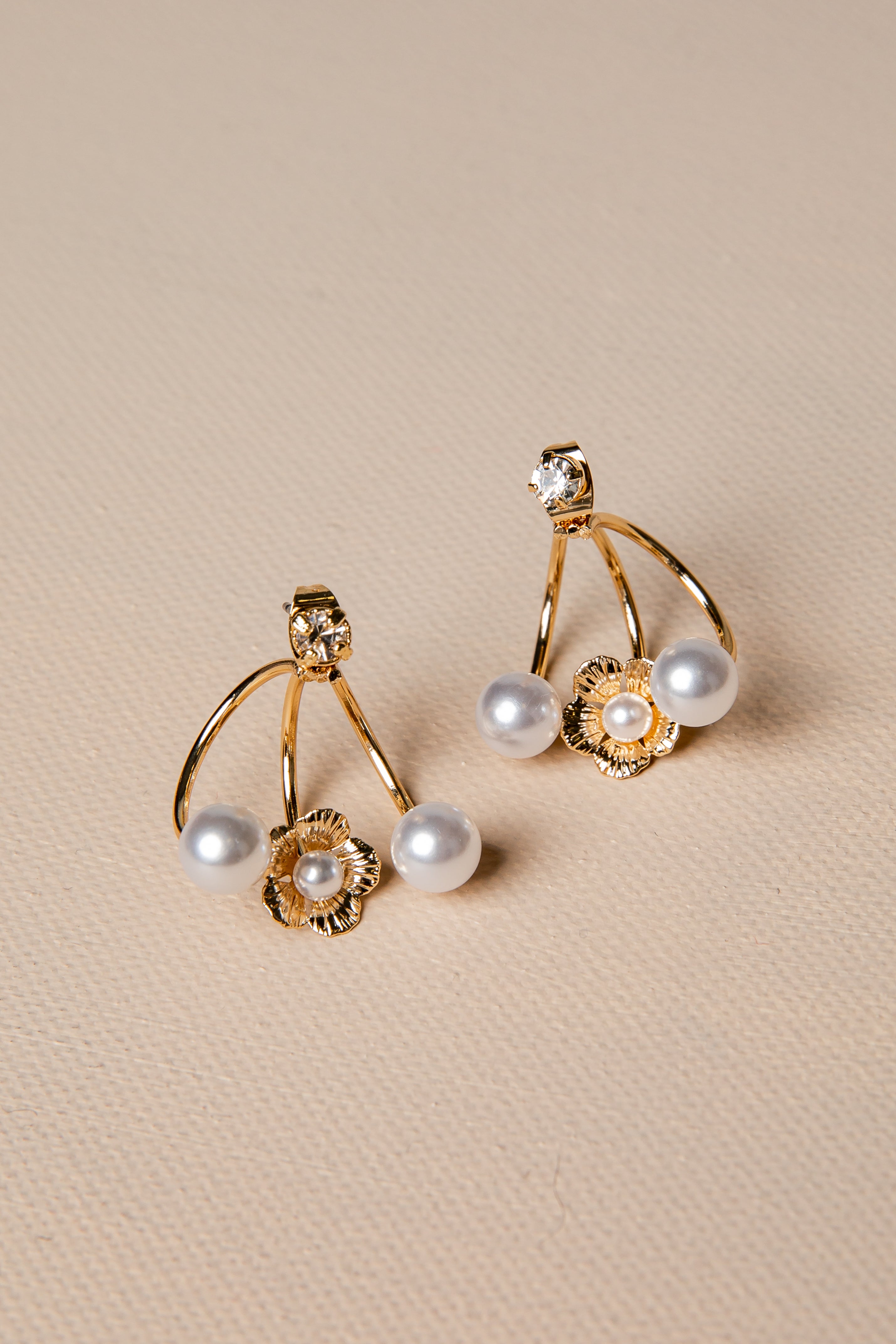 Gold hoop earrings with pearl accents on a beige background