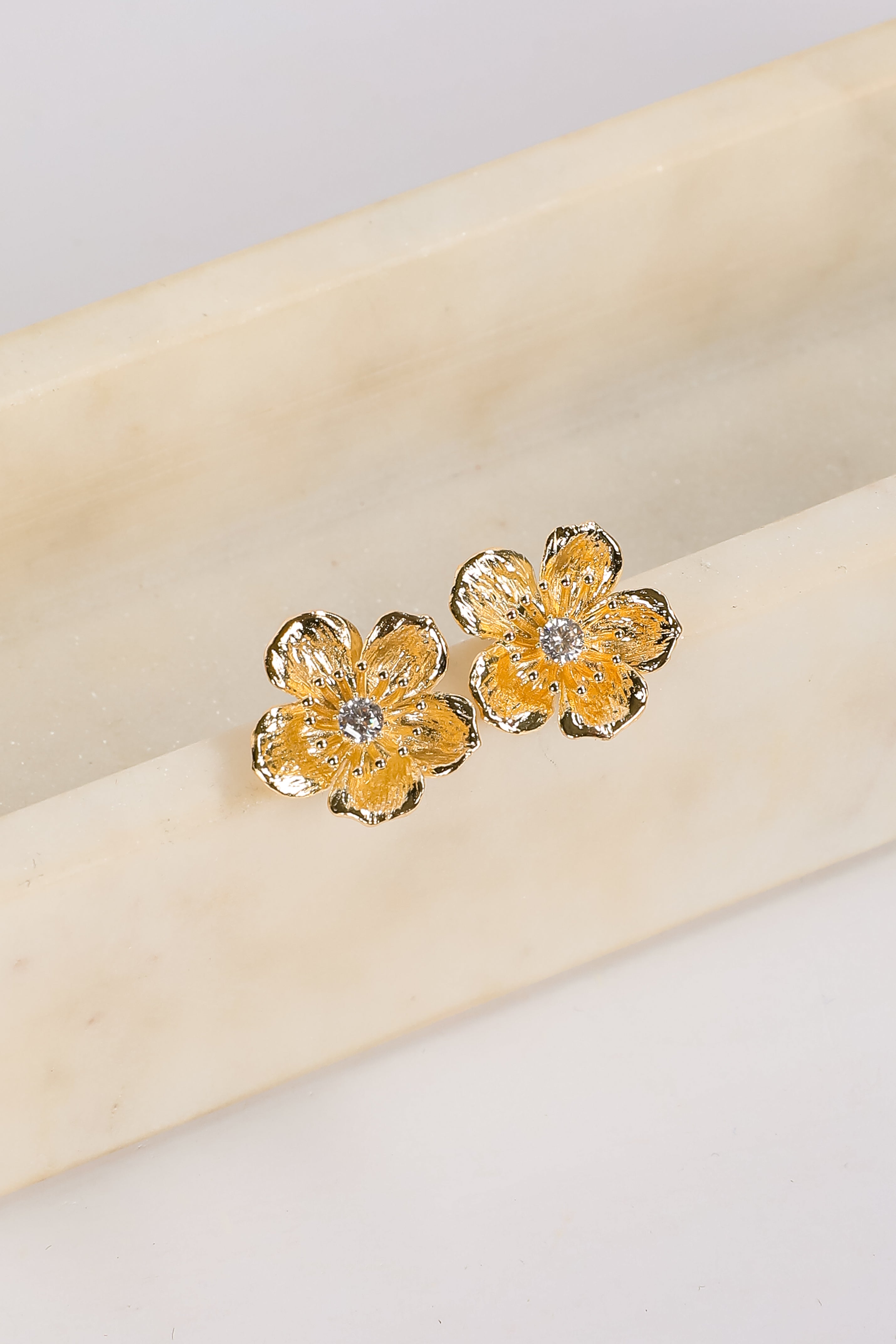Gold flower-shaped earrings with a central gemstone on a beige fabric background
