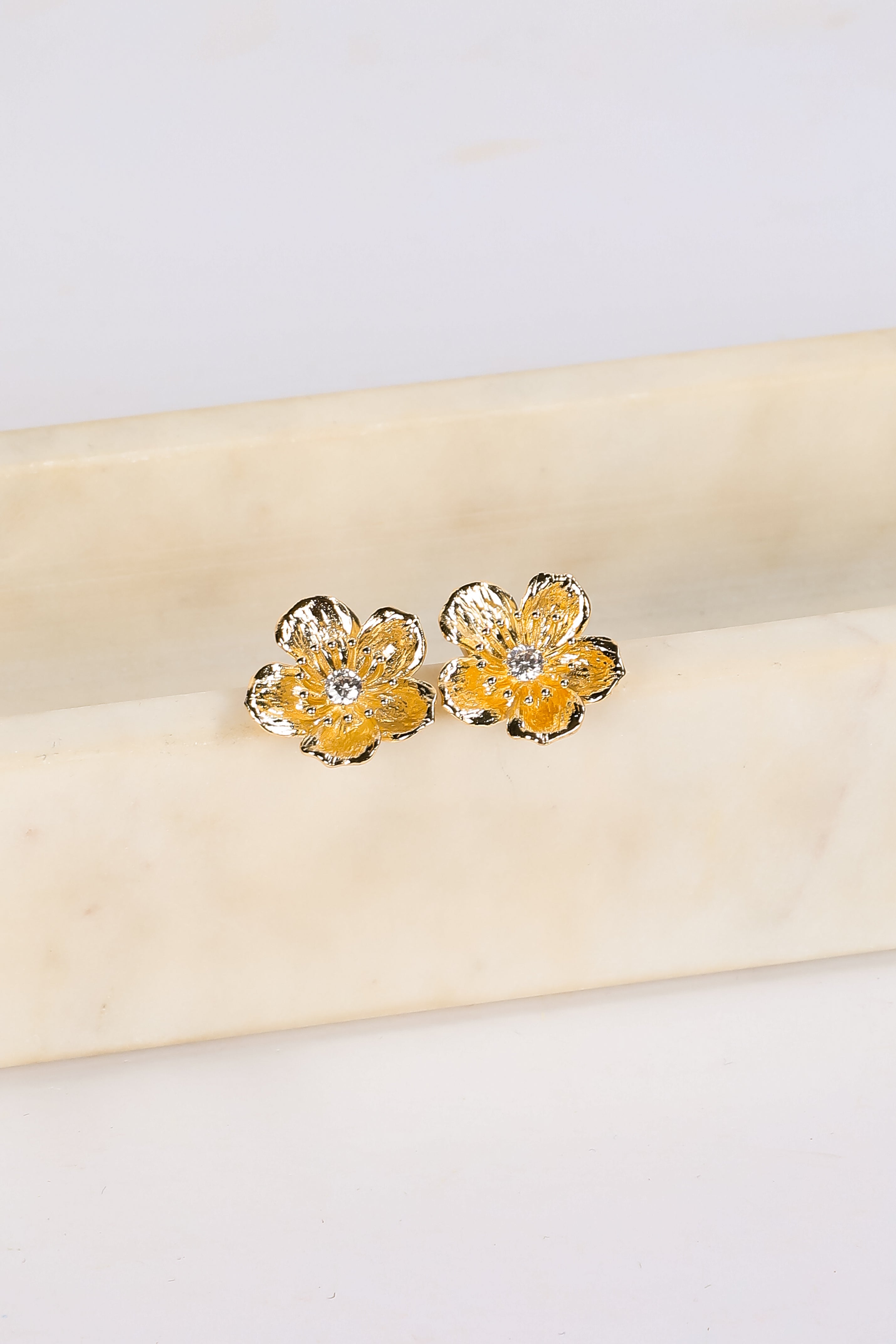 Gold flower-shaped earrings on a beige fabric background