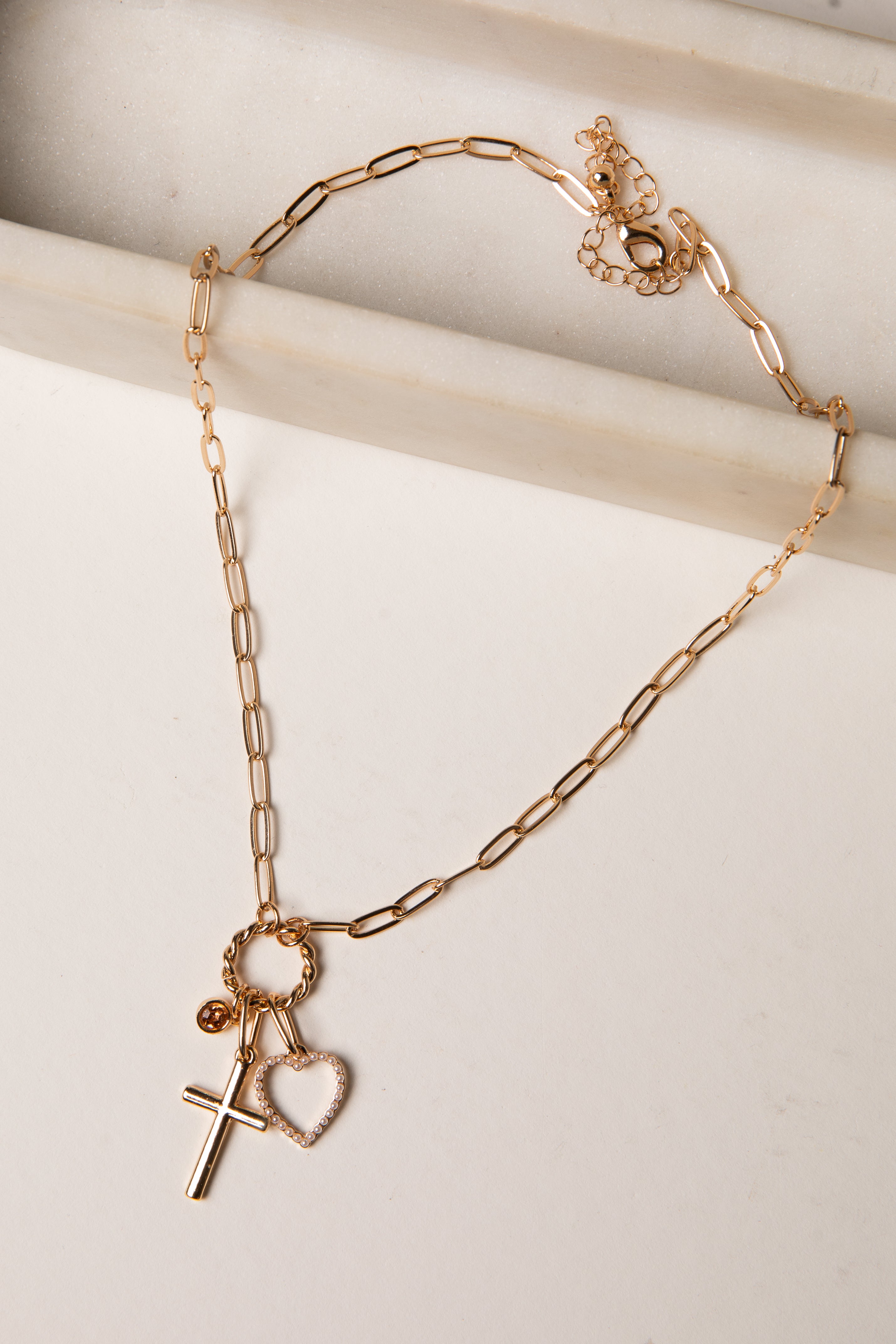Gold chain bracelet with heart and cross charms on a light background