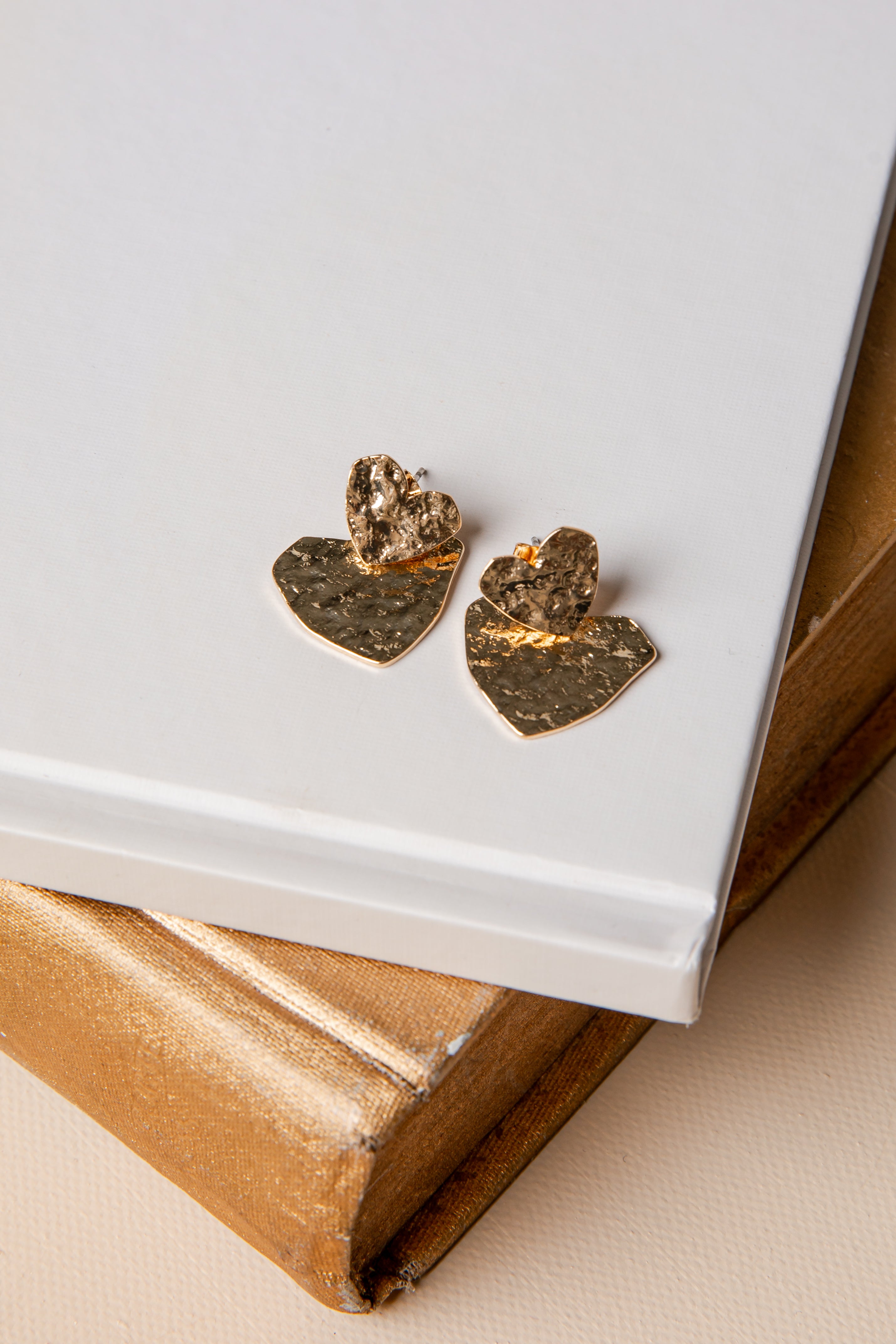Pair of gold and bronze heart-shaped earrings on a white surface with a beige background