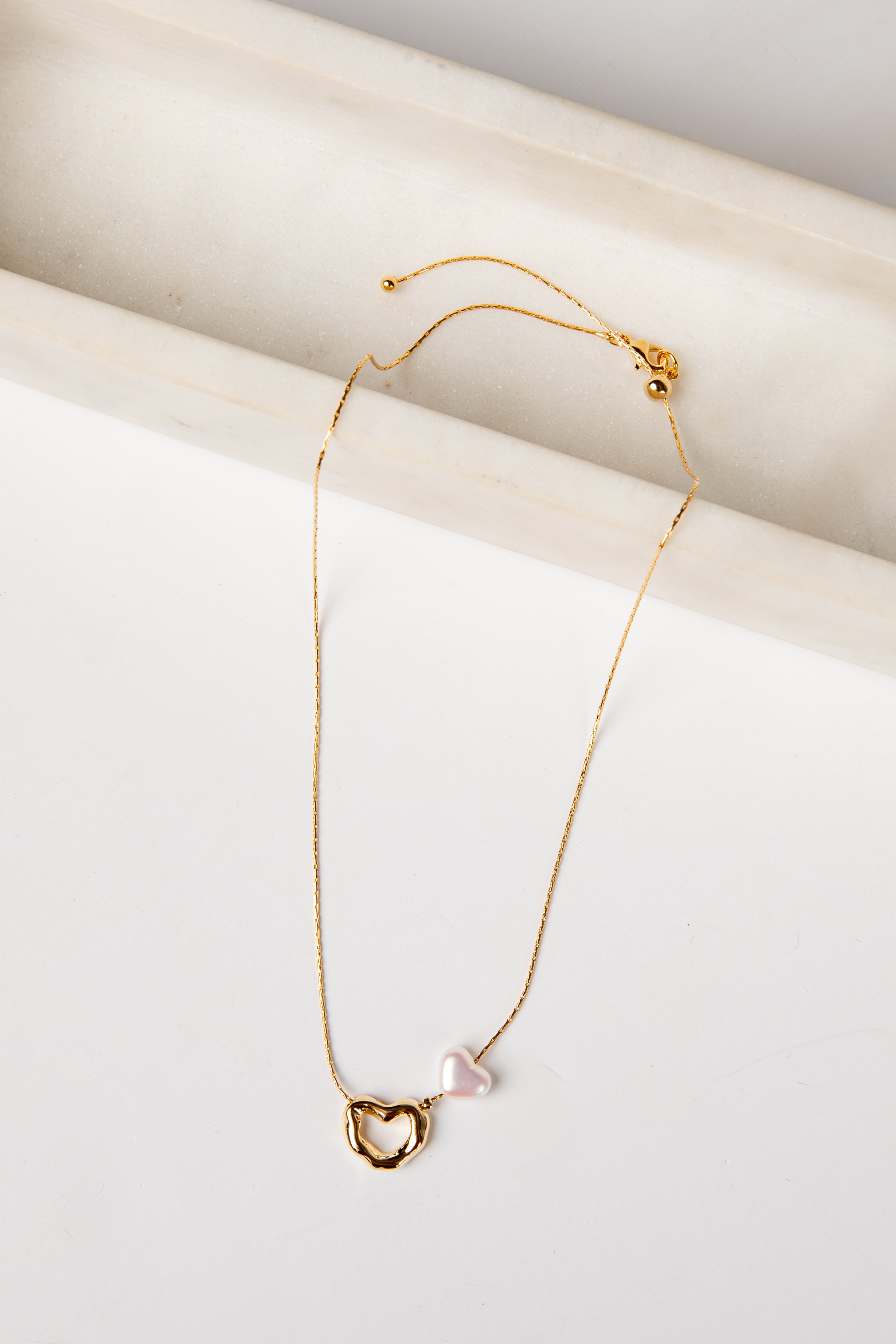 Gold necklace with a heart-shaped pendant on a white surface