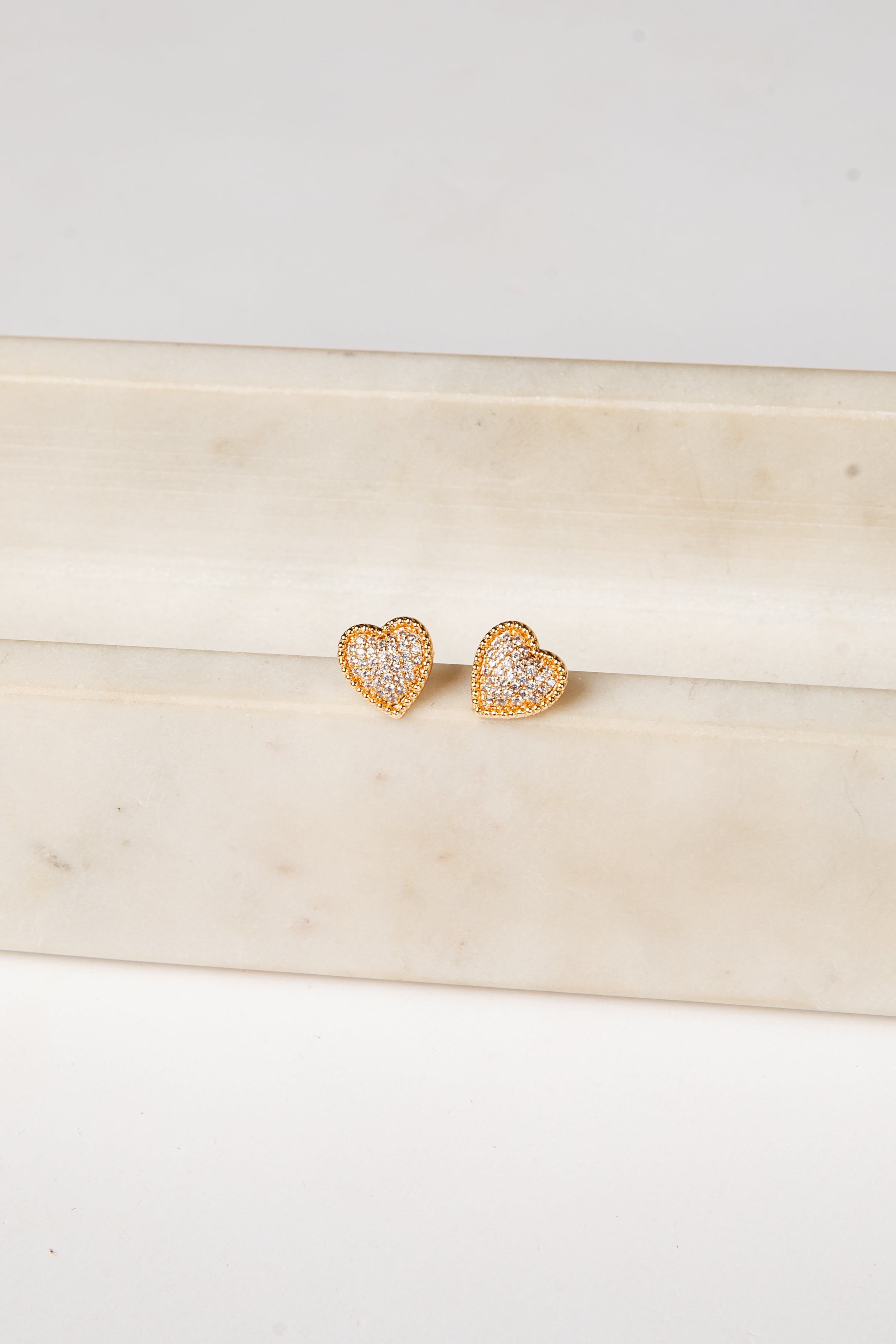 Heart-shaped earrings with clear stones on a light wooden surface