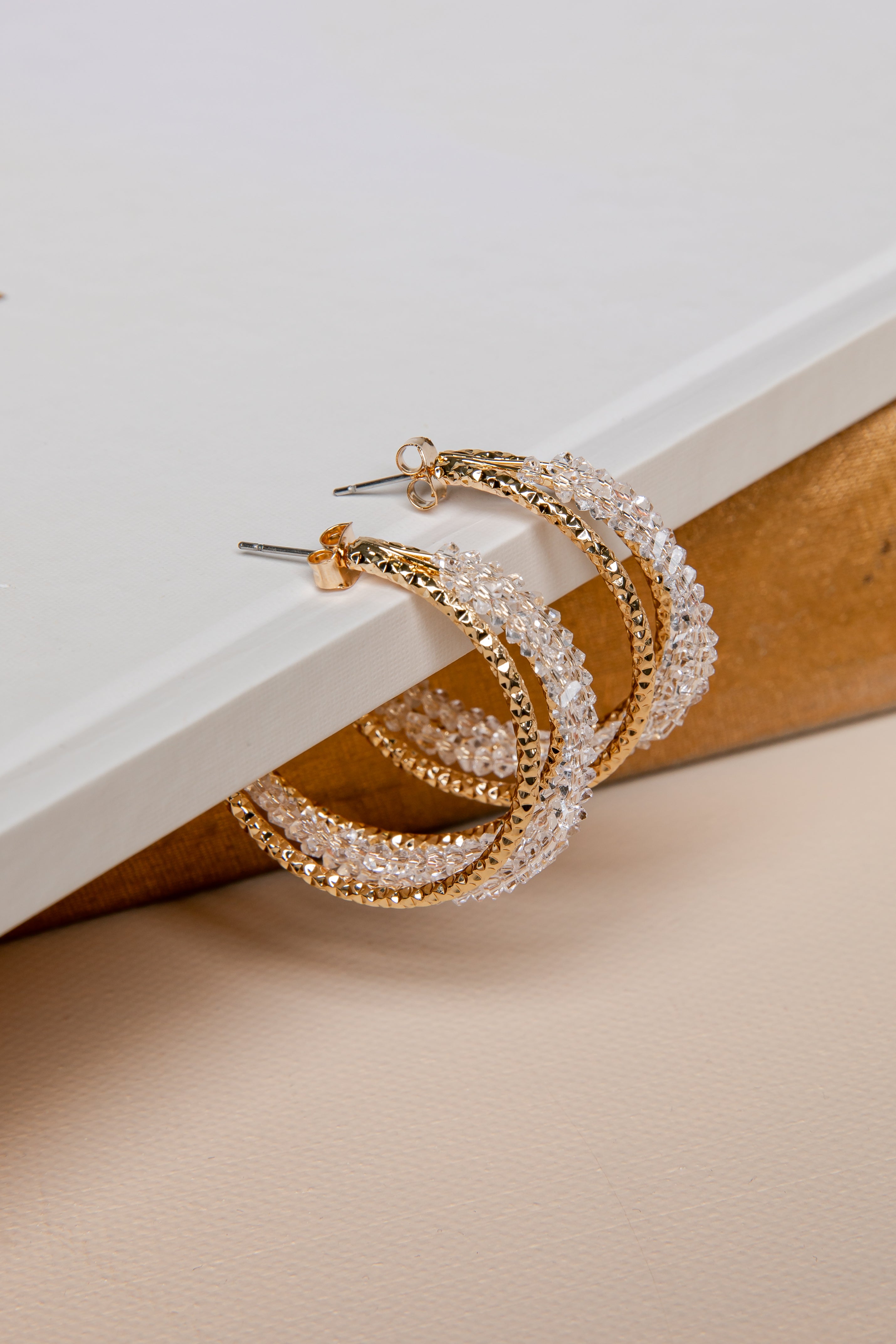 Gold and crystal hoop earrings on a beige surface with a white background