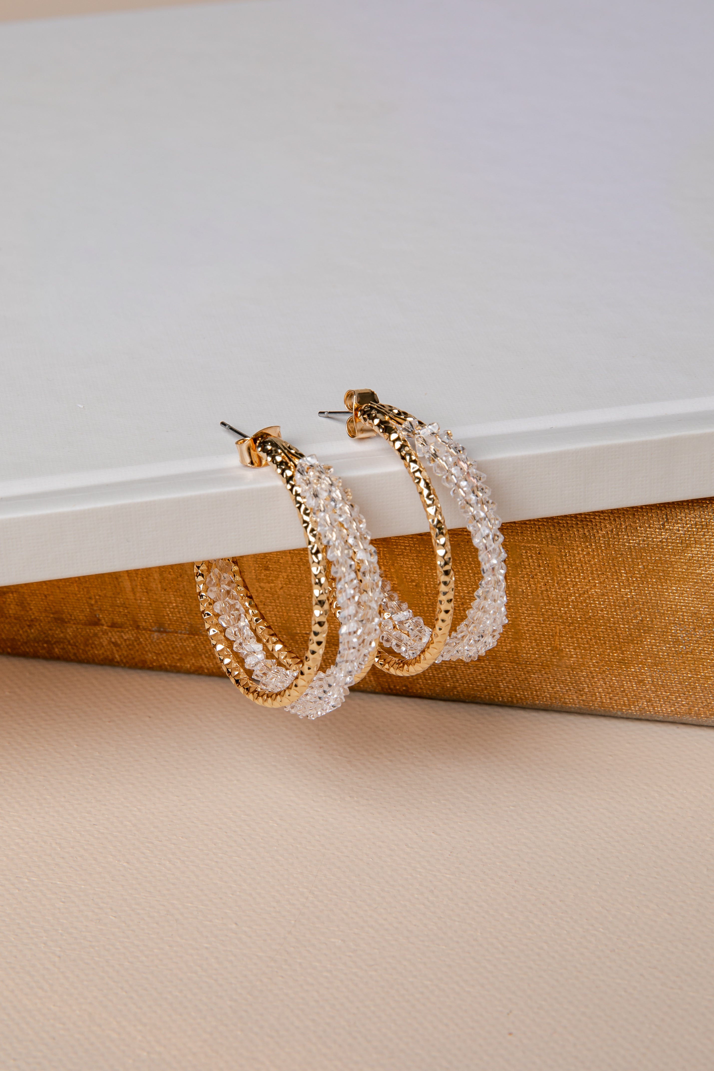 Pair of gold and pearl hoop earrings on a textured surface with a neutral background