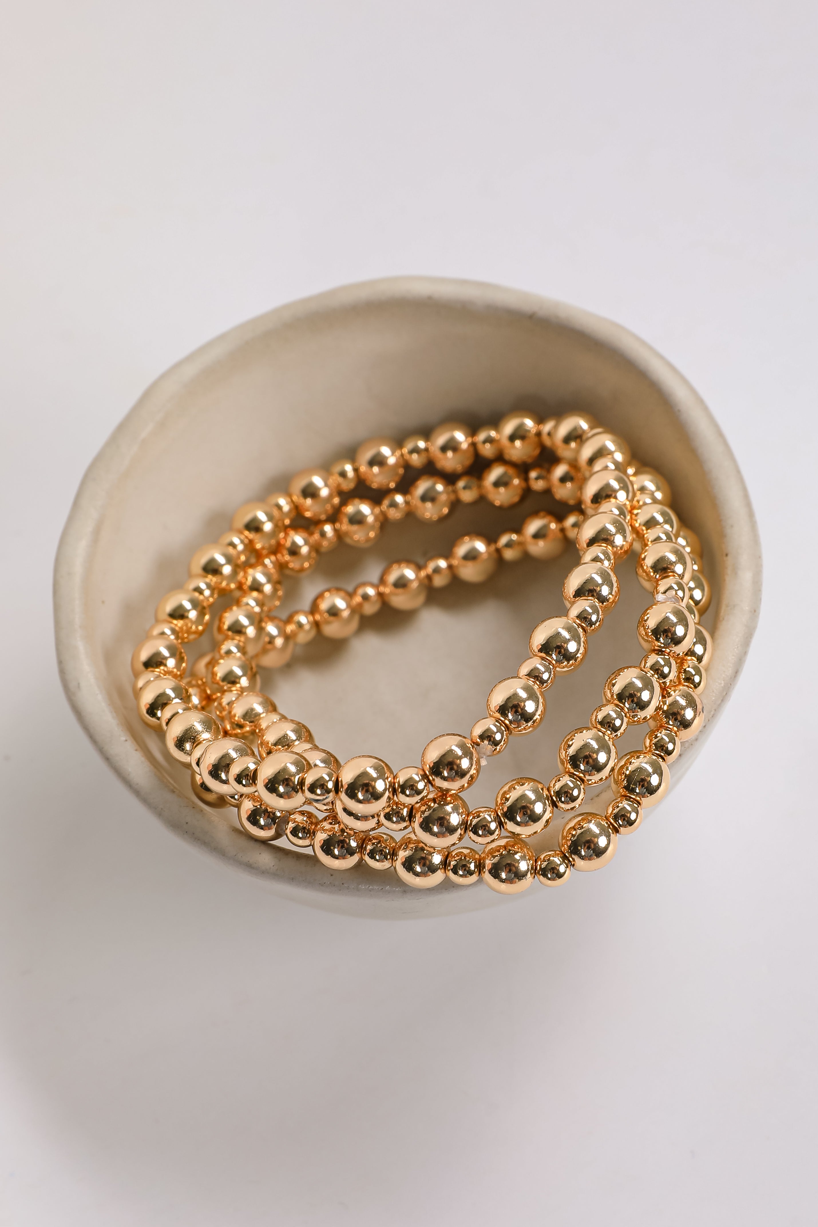 Gold beaded bracelets on a beige dish with a white background