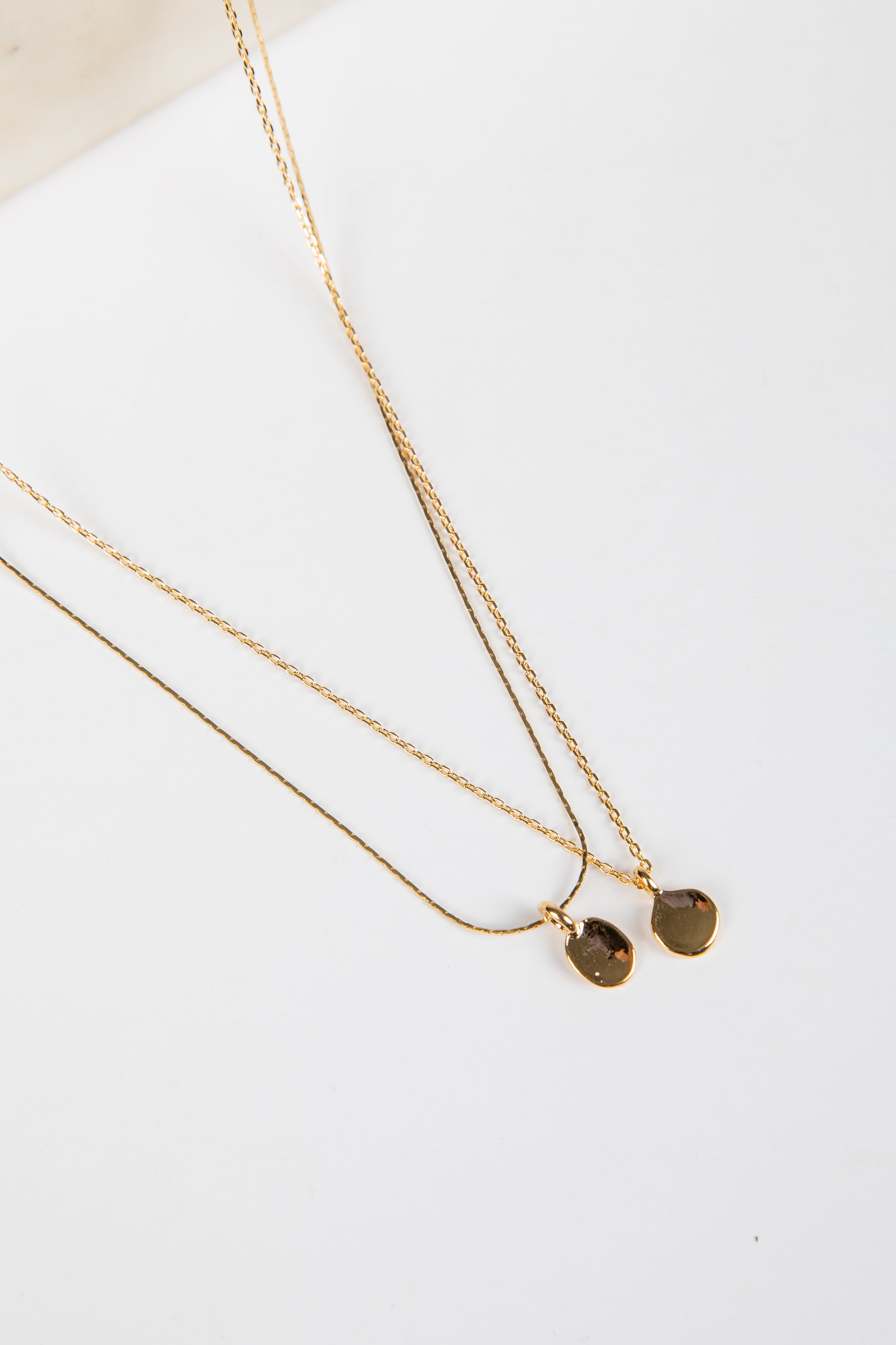 Two gold necklaces with pendant drops on a white surface