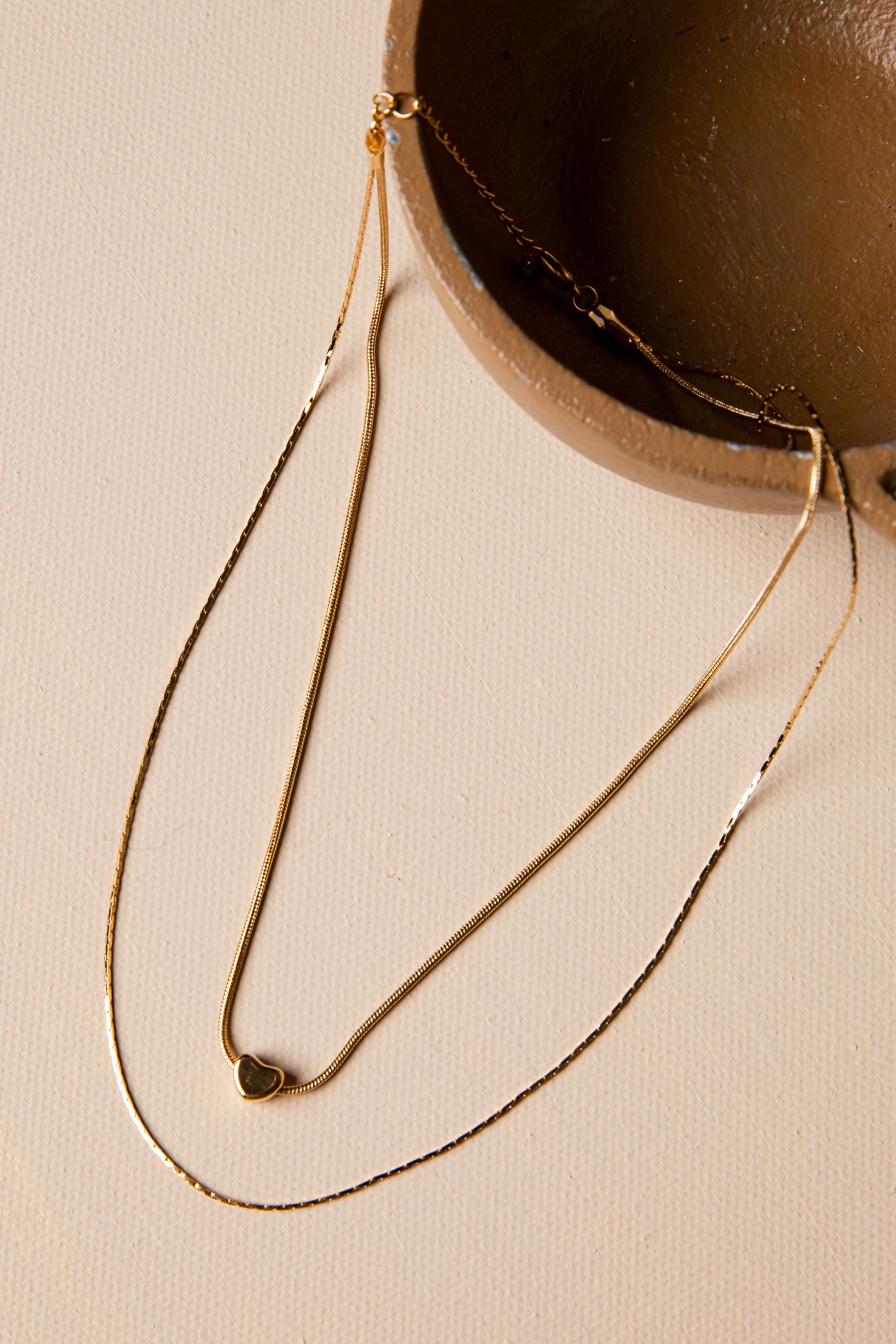 Gold necklace with a heart pendant on a beige surface