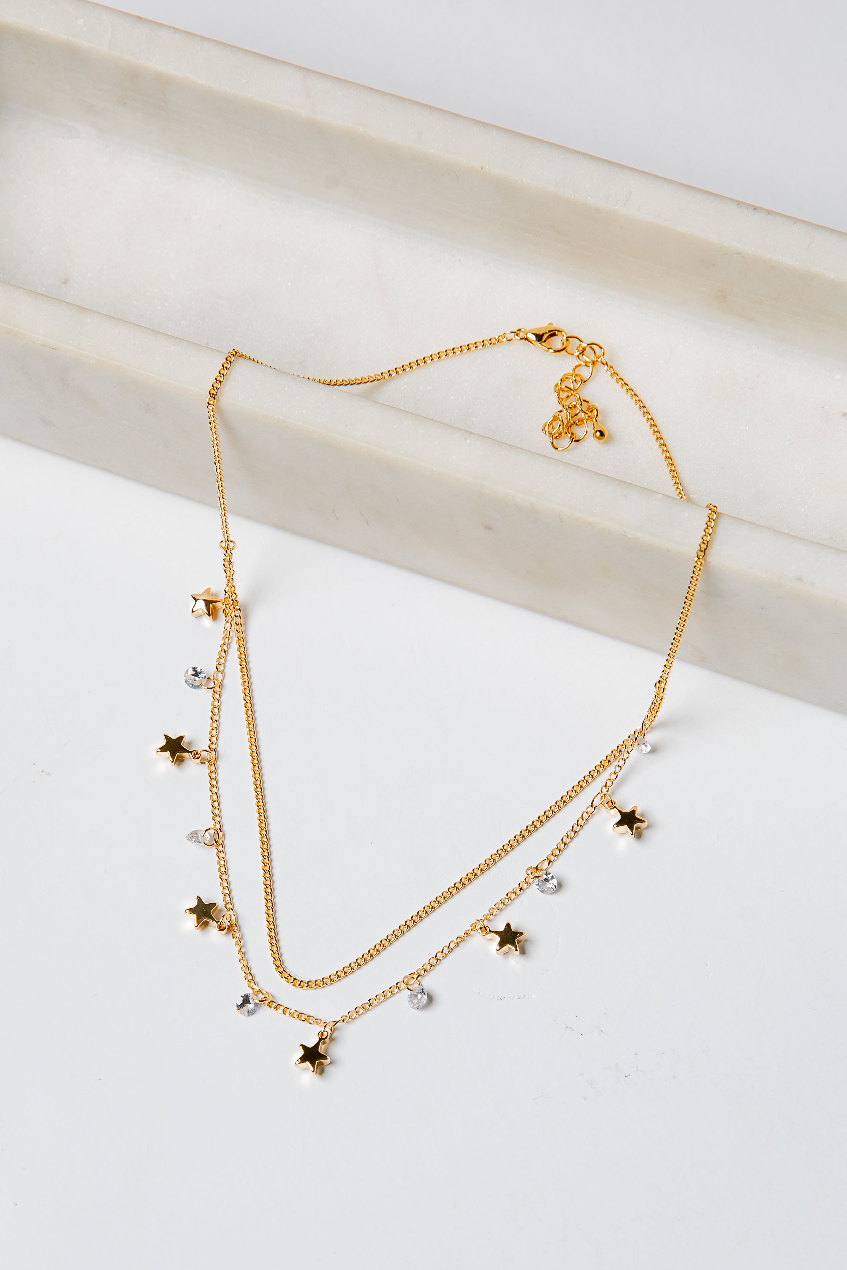 Gold layered necklace with star and heart pendants on a light background