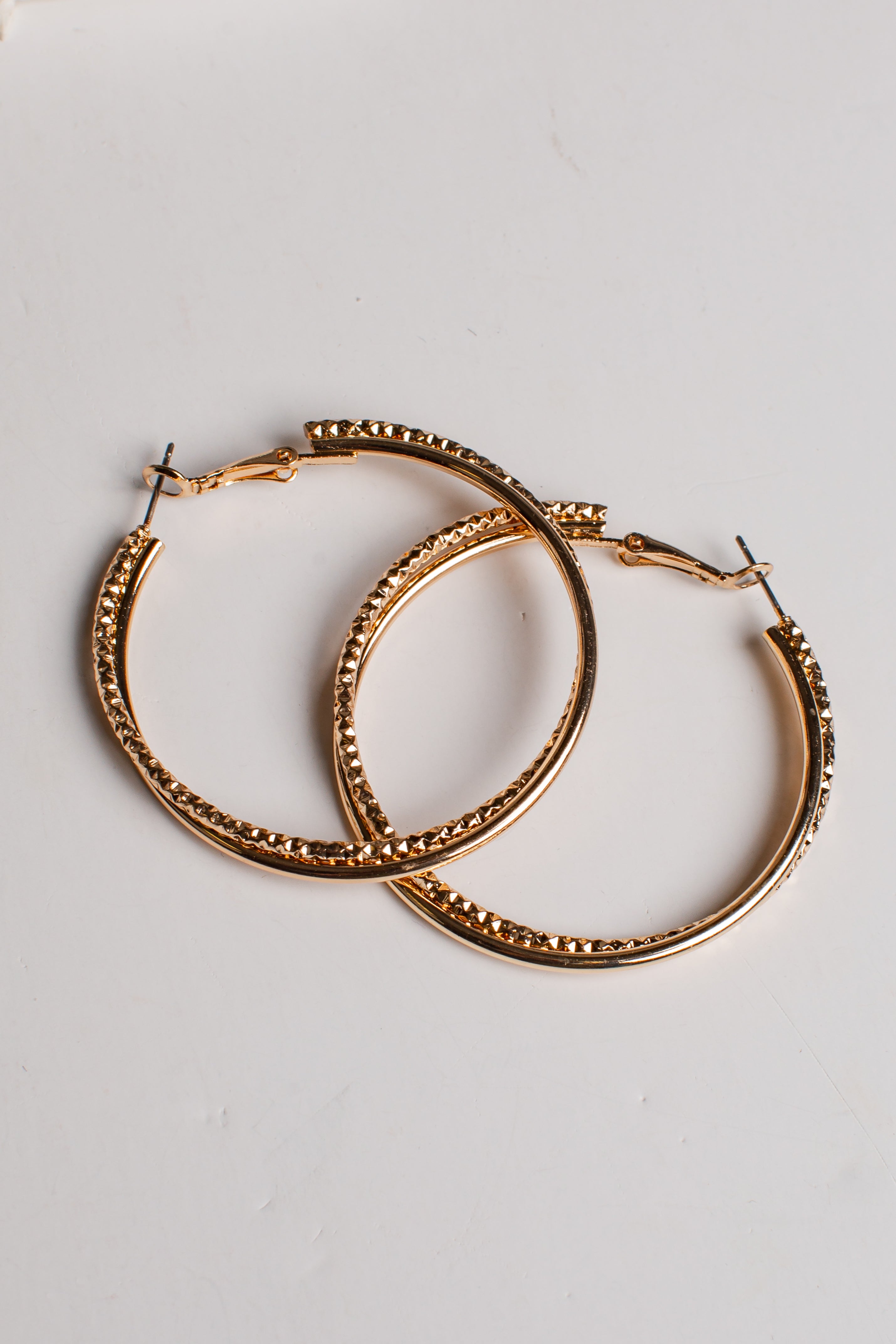 A pair of gold-tone hoop earrings with a textured, beaded outer edge and solid inner bands, displayed on a clean white background.