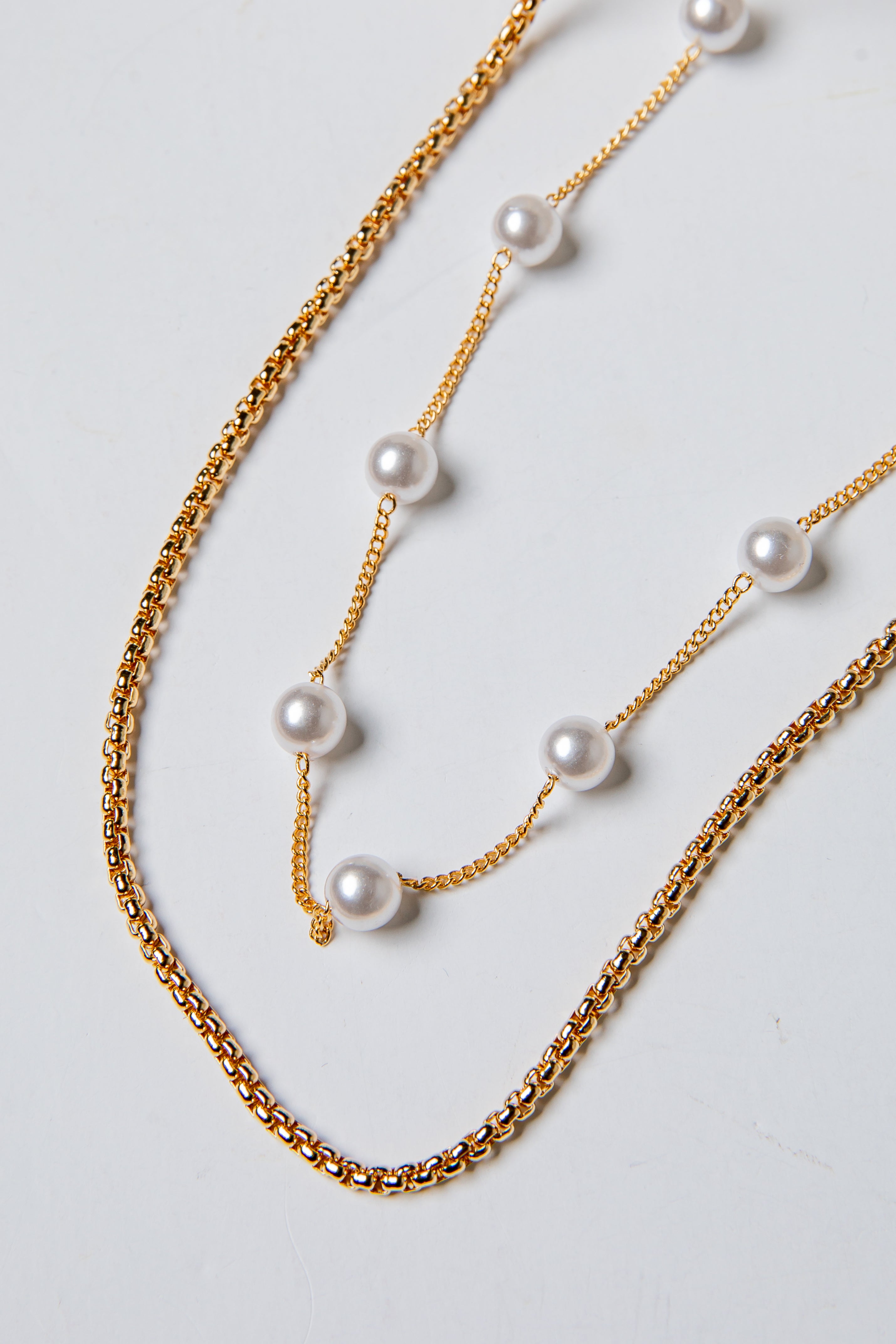 Two gold chain necklaces with pearls on a light gray background