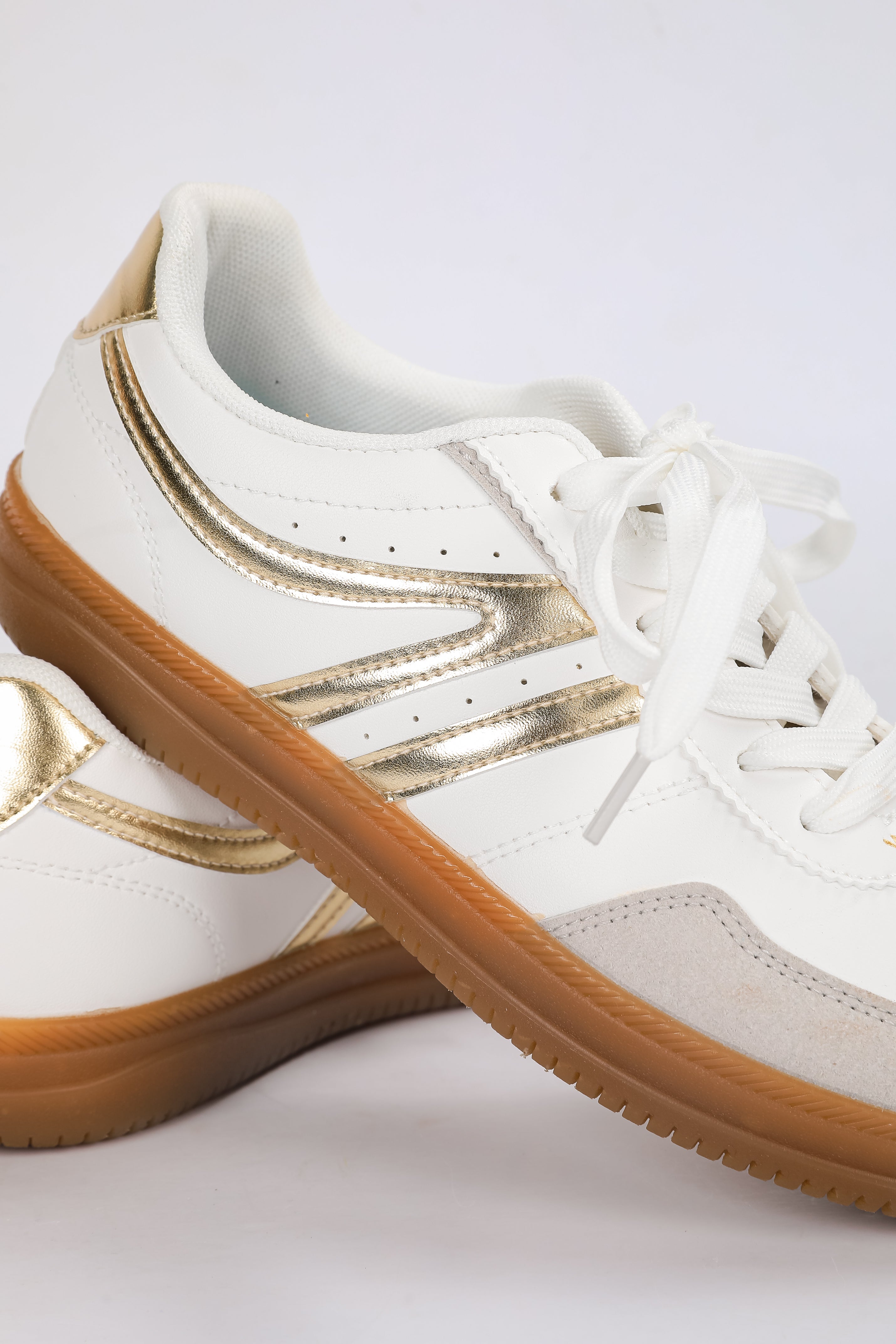White sneakers with gold accents and brown soles on a white background