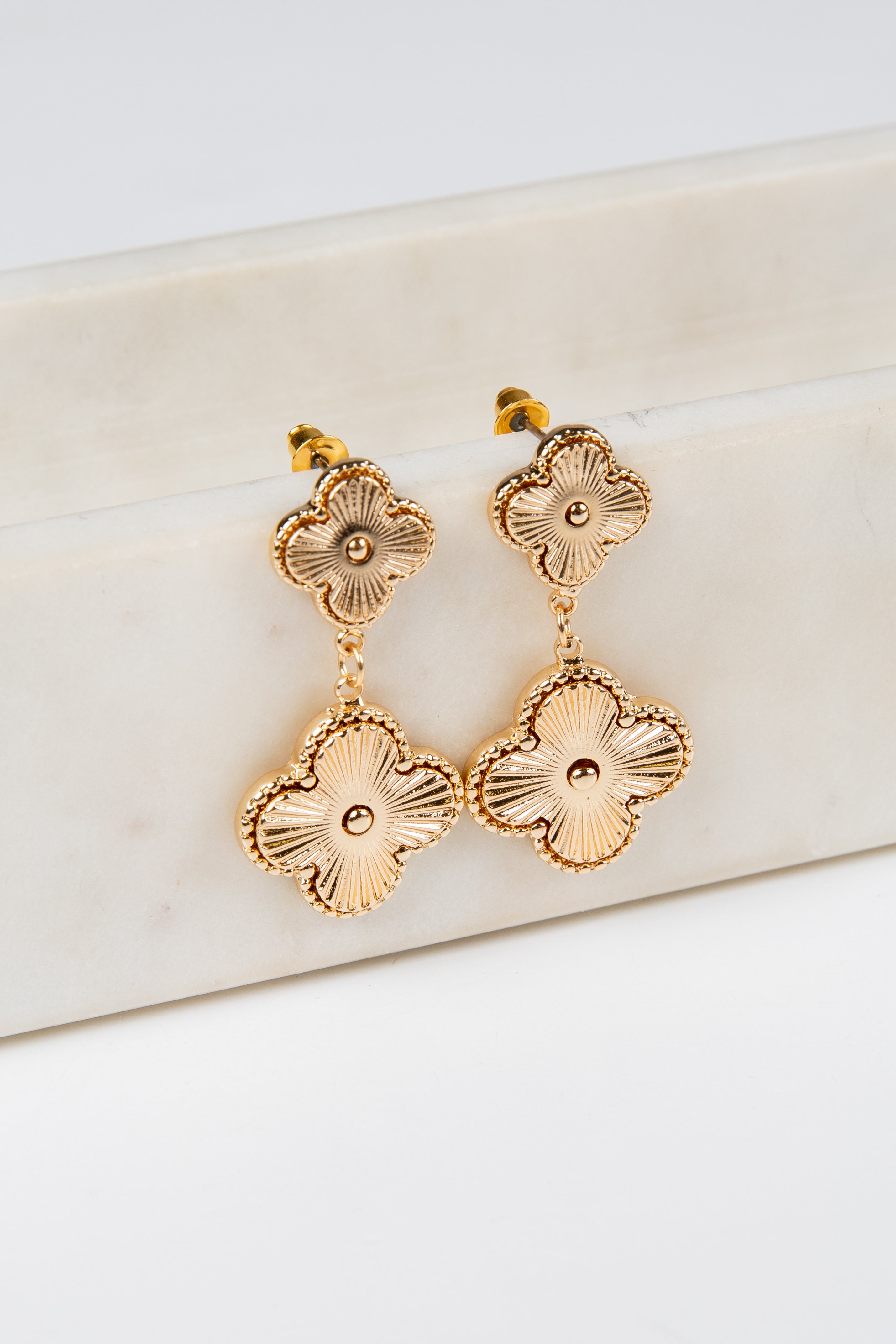 Gold floral earrings on a white marble surface