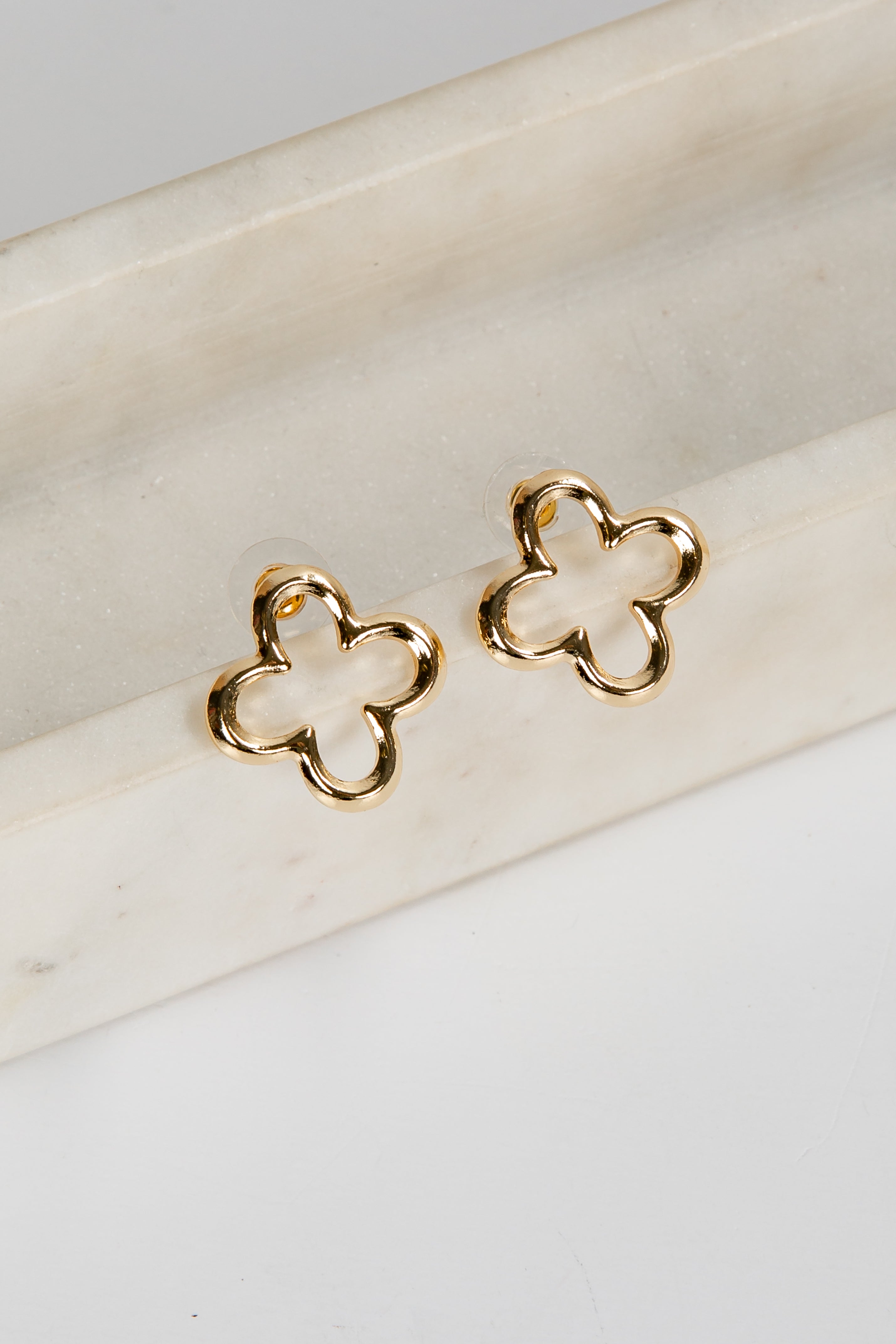 Gold clover-shaped earrings on a white surface
