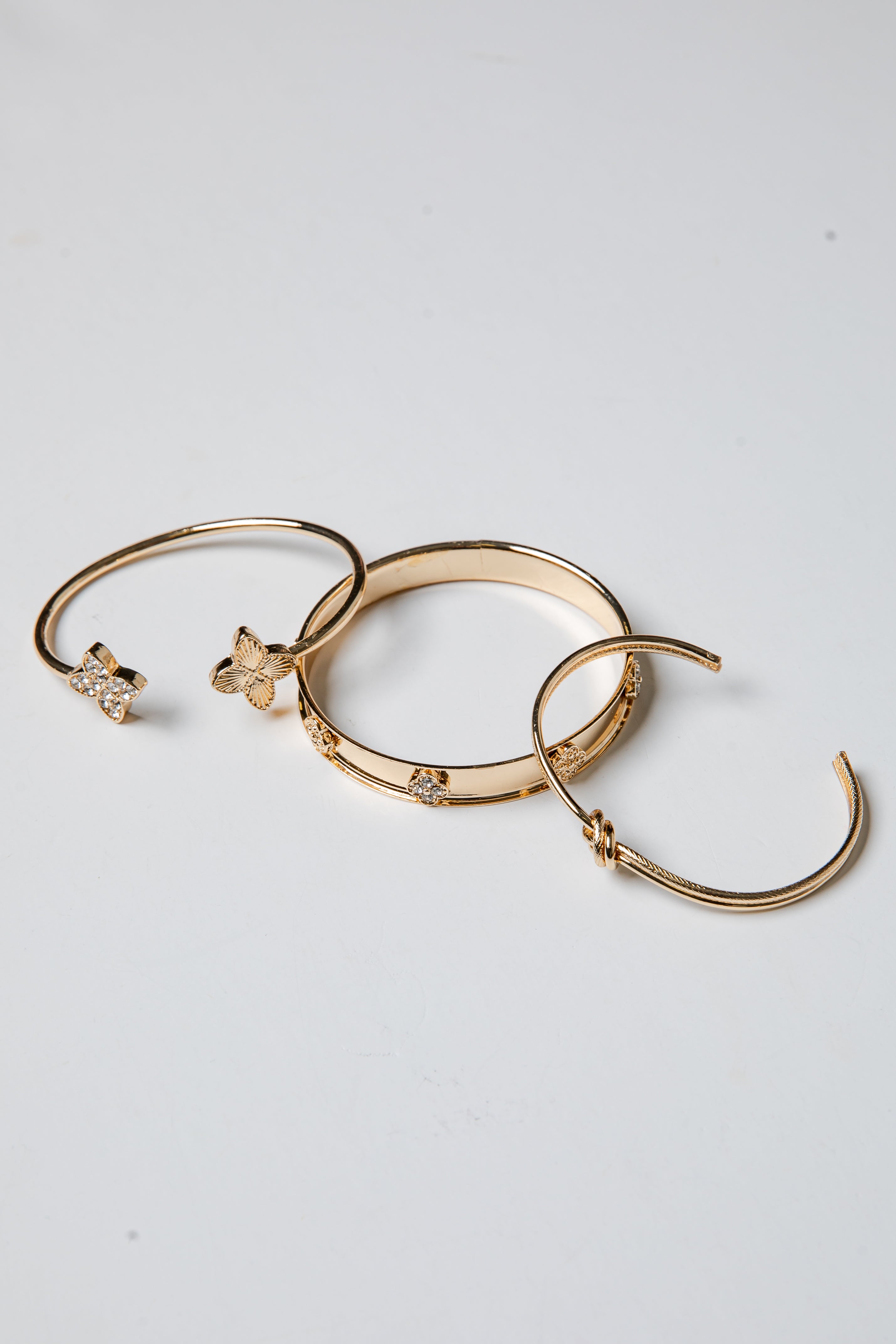 Three gold bracelets with decorative elements on a light gray background