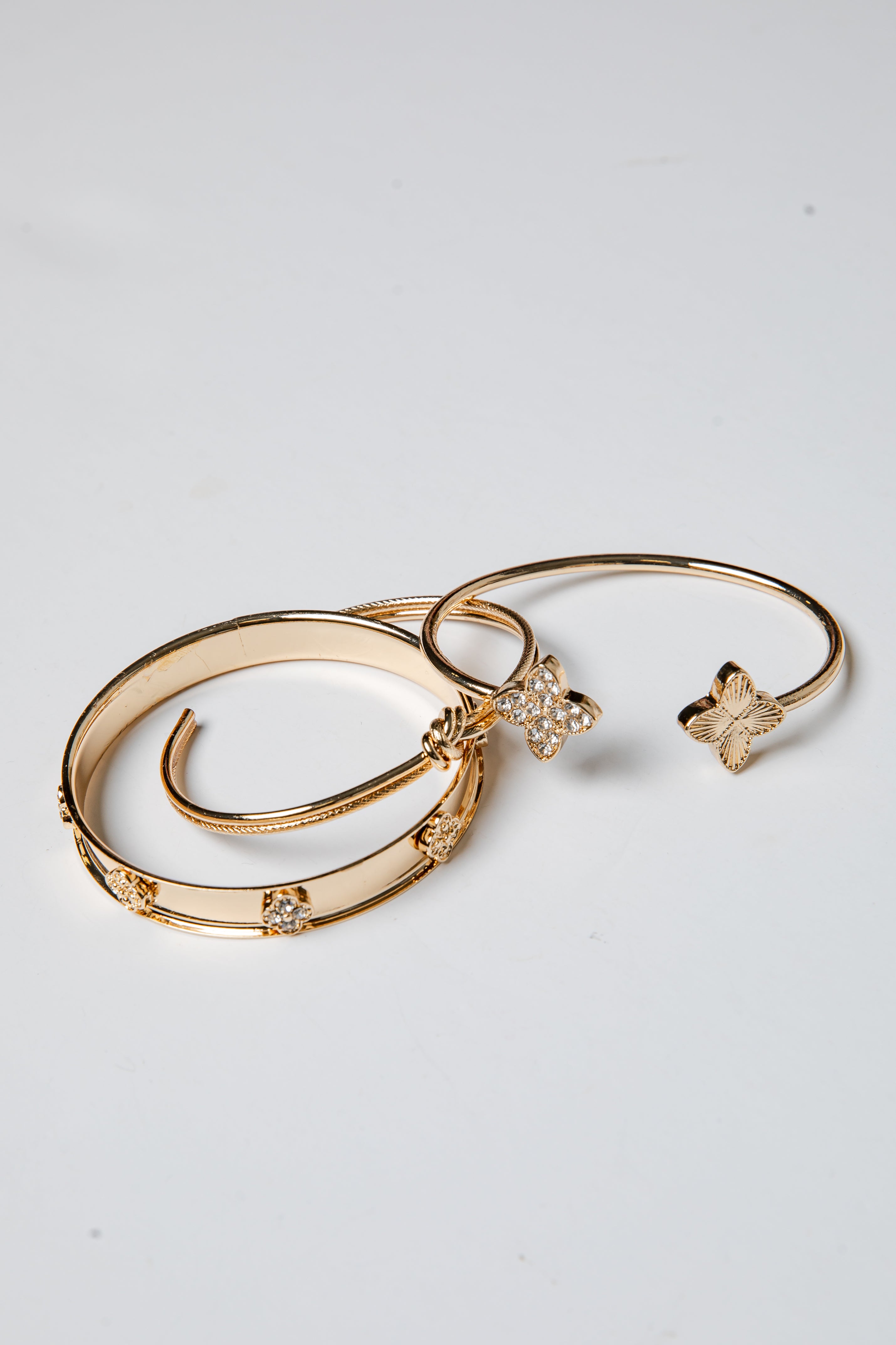 Three gold bracelets with butterfly charms on a light gray background