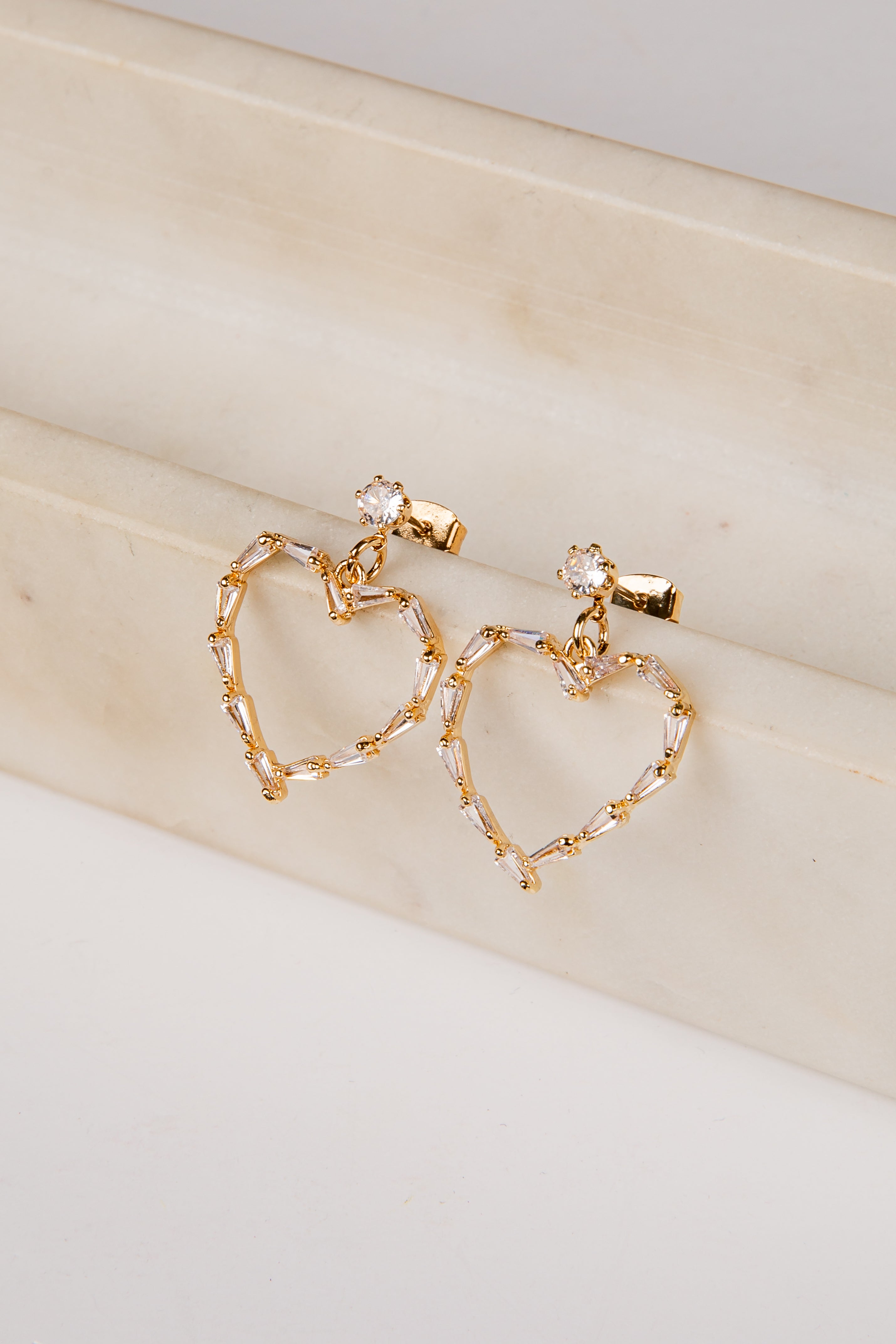 Gold heart-shaped earrings on a beige surface