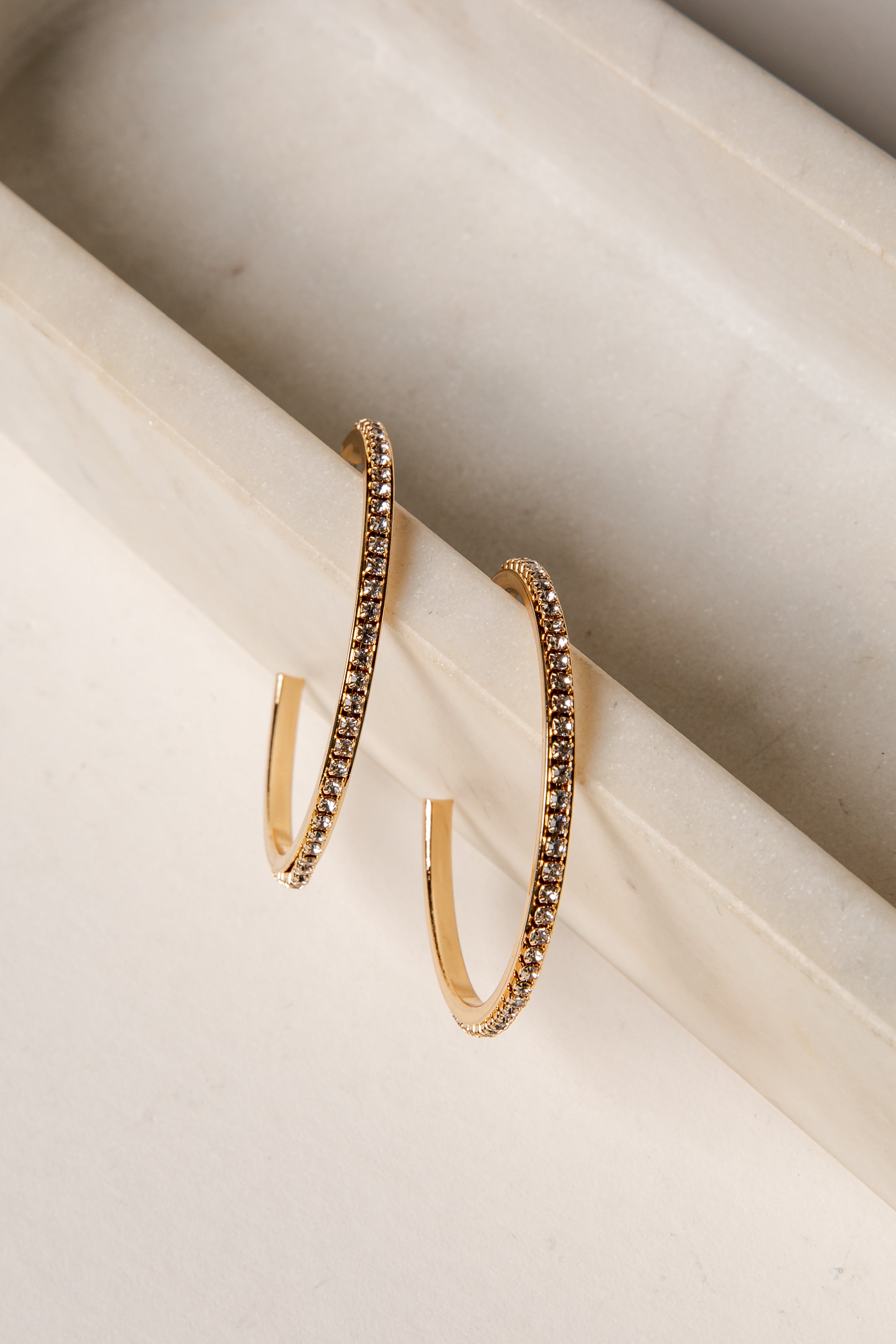 Gold hoop earrings with embedded stones on a marble surface